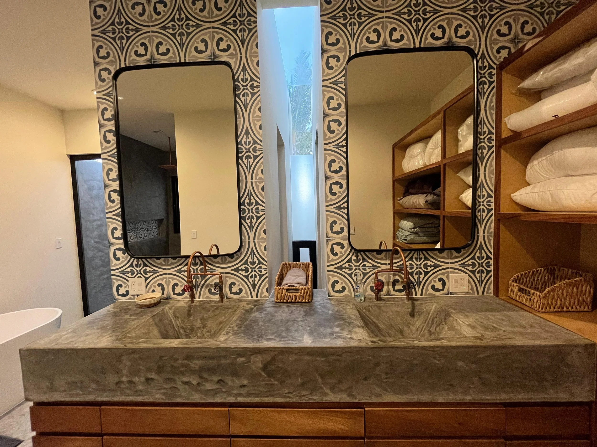 Double vanity bathroom with two large mirrors, a grey marble countertop, and a wooden cabinet with woven baskets and linens.