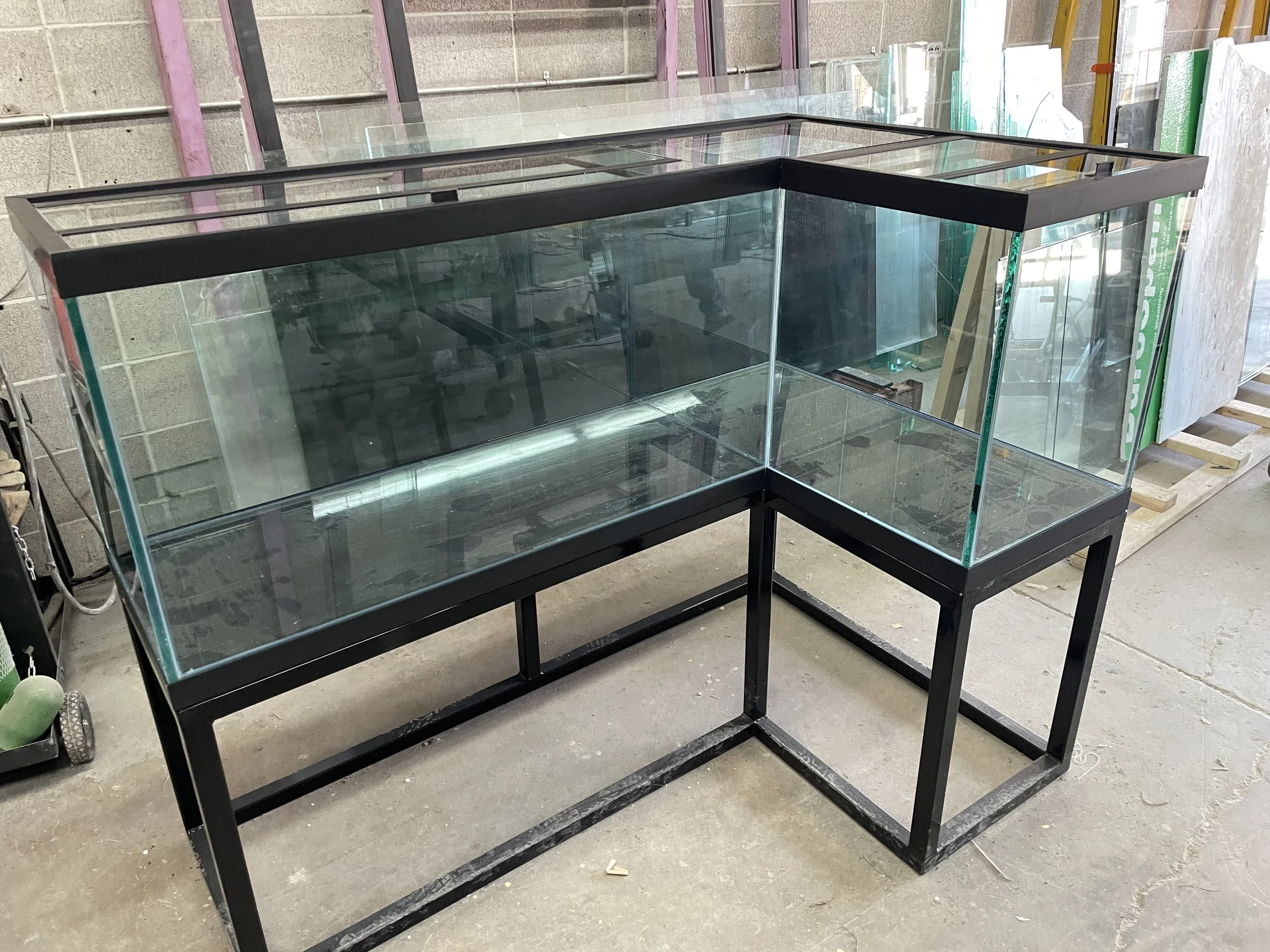 Empty glass display case with black frame on a concrete floor in a warehouse.