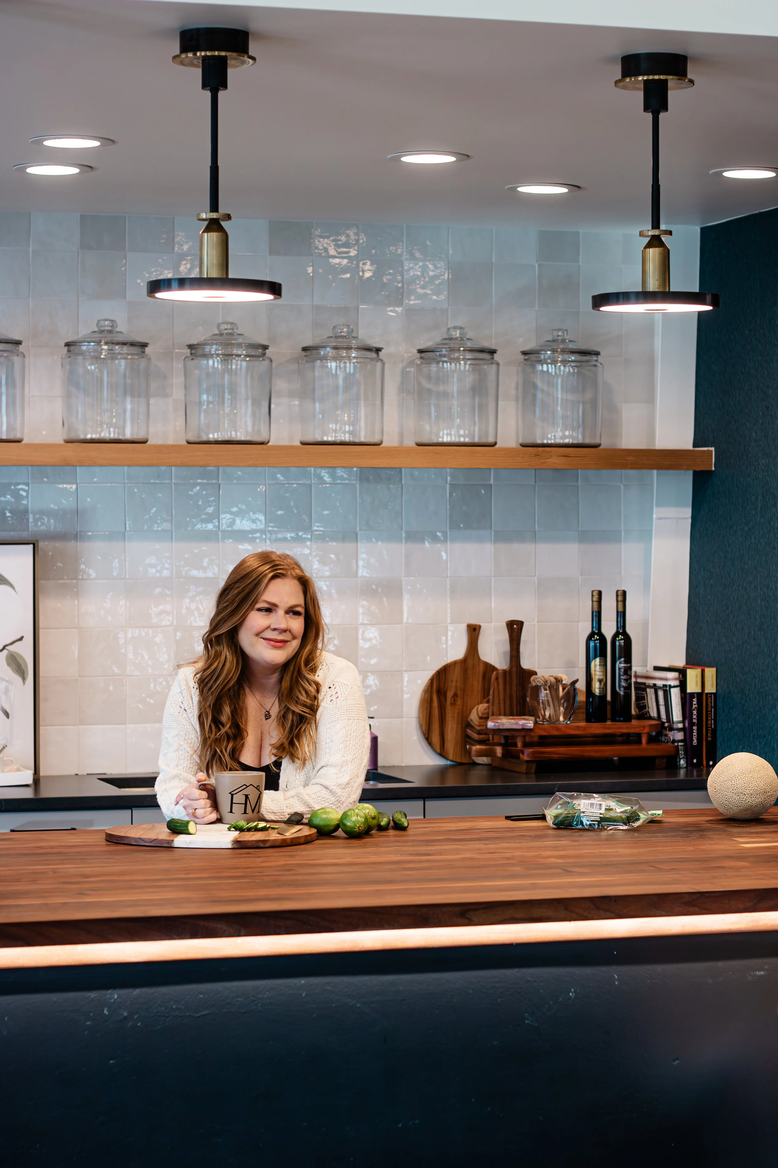 A family nutritionist sitting in a modern kitchen with a mug, surrounded by fresh cucumbers and limes on the counter, reflecting a real-life approach to kids’ and family nutrition.