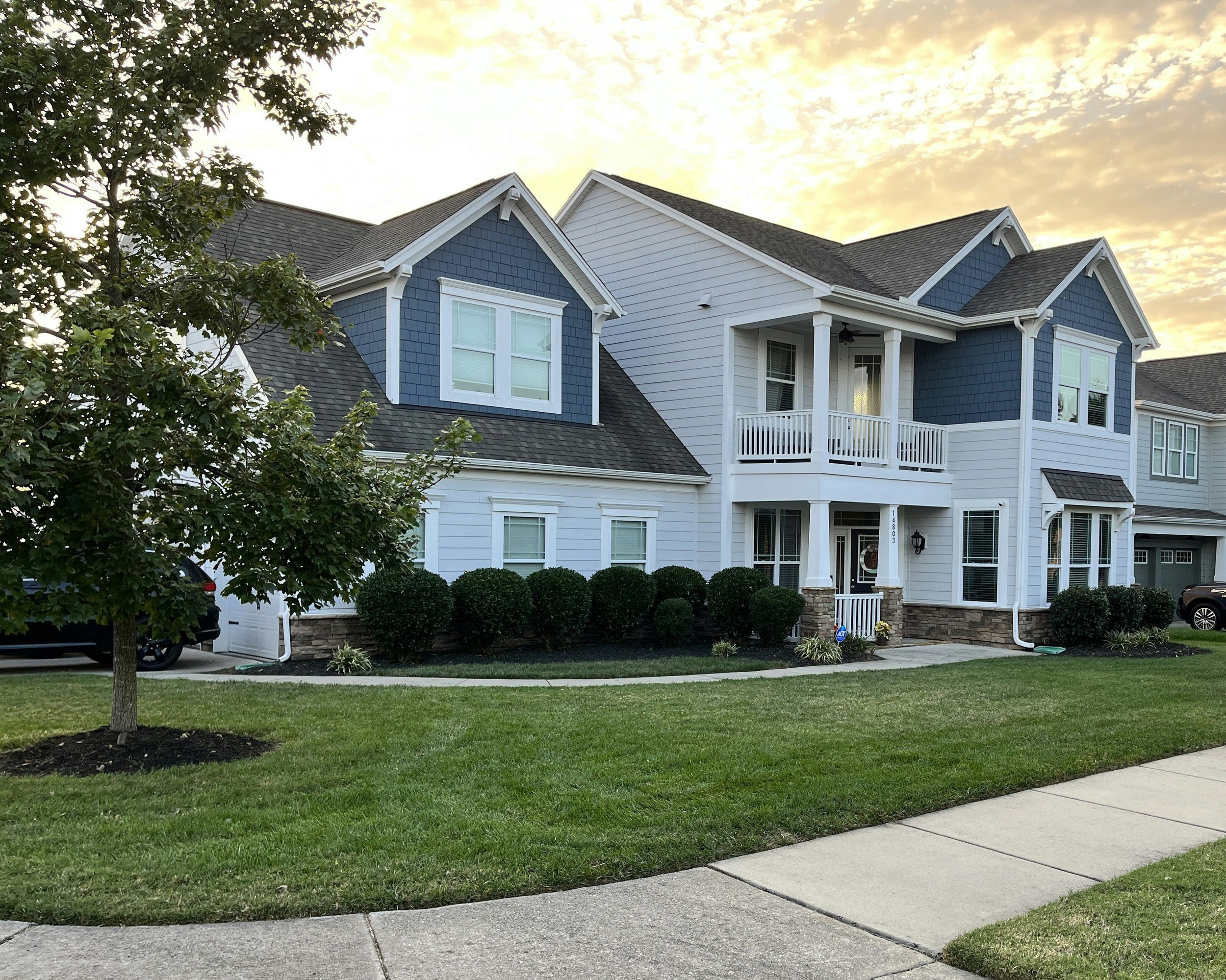 A two-story house with a white and blue exterior, front porch, and well-kept lawn at sunset.