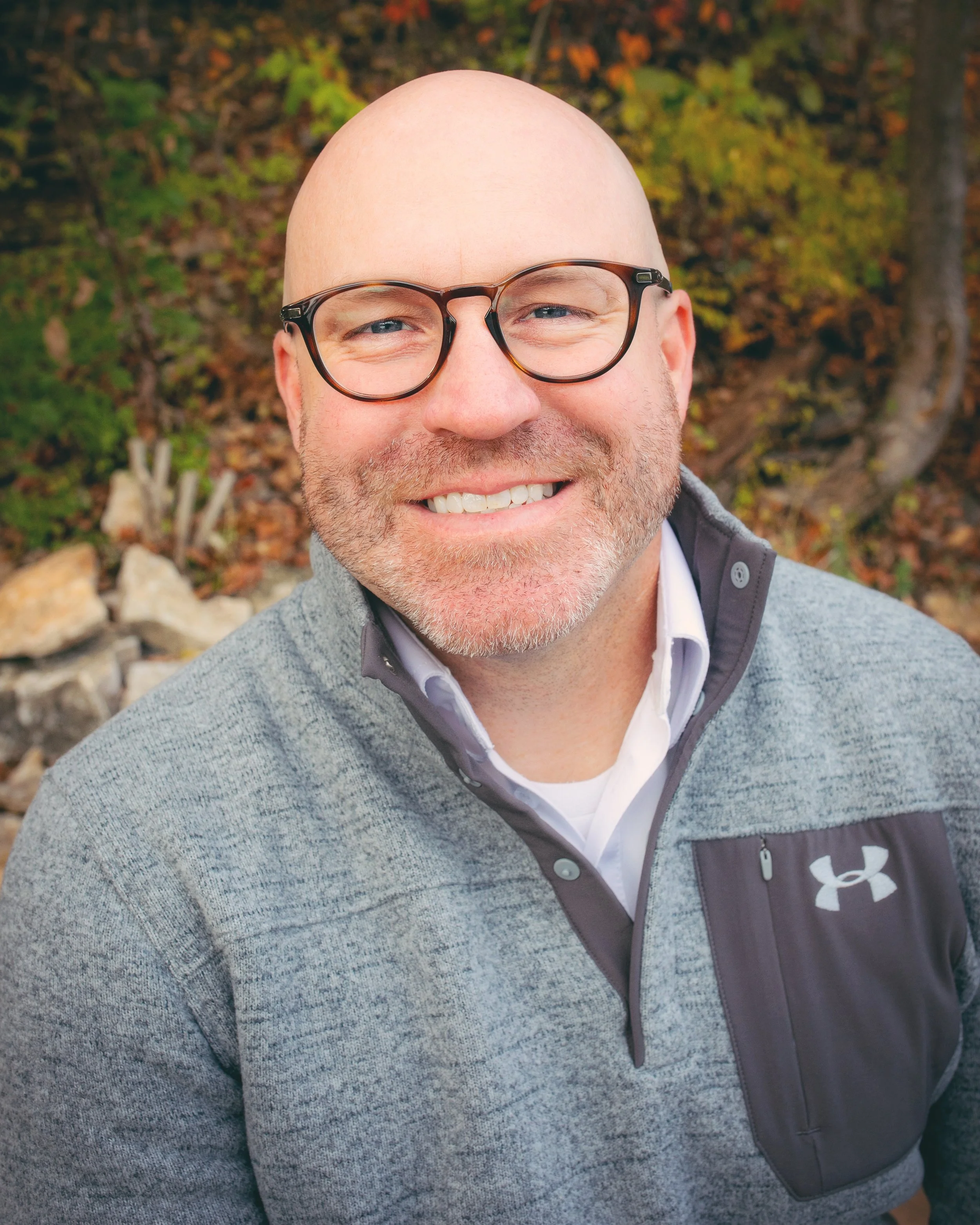 Author Kaleb Stoppel smiling outdoors, wearing glasses and a gray pullover.