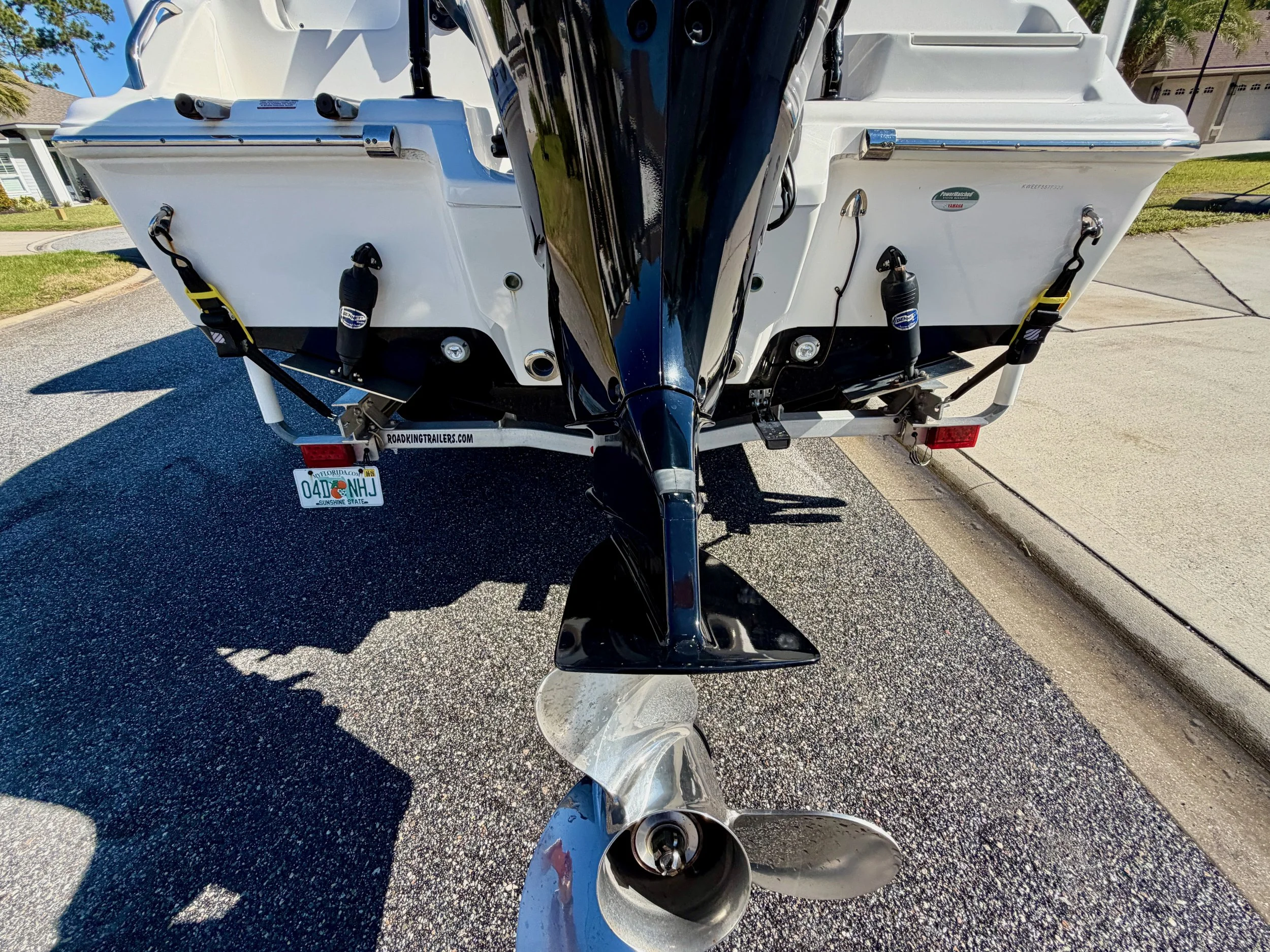 Rear view of a white motorboat on a trailer, showing the outboard motor and propeller, parked on a residential street.
