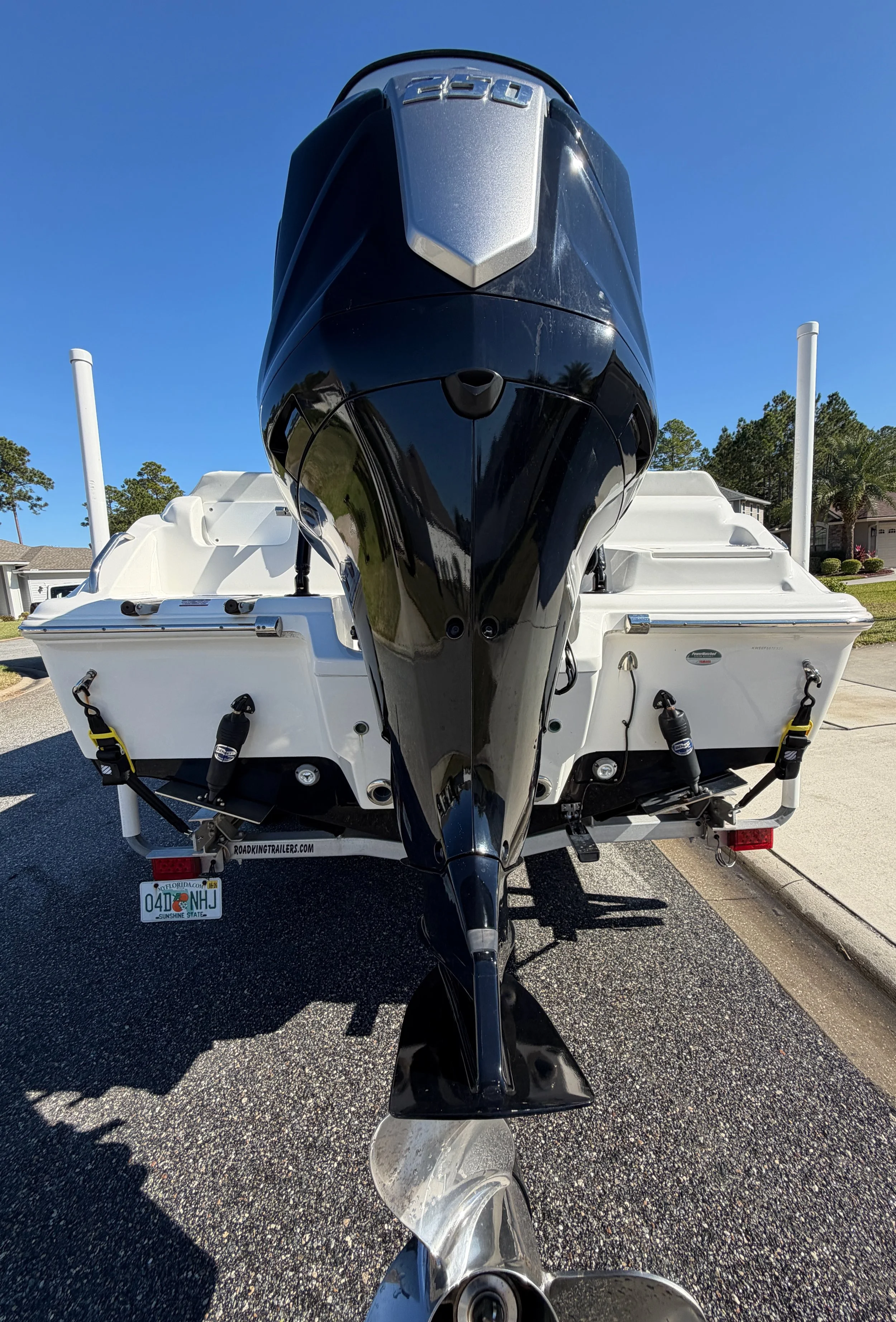 Front view of a white boat with a black outboard motor, parked on a trailer on a driveway during daytime.