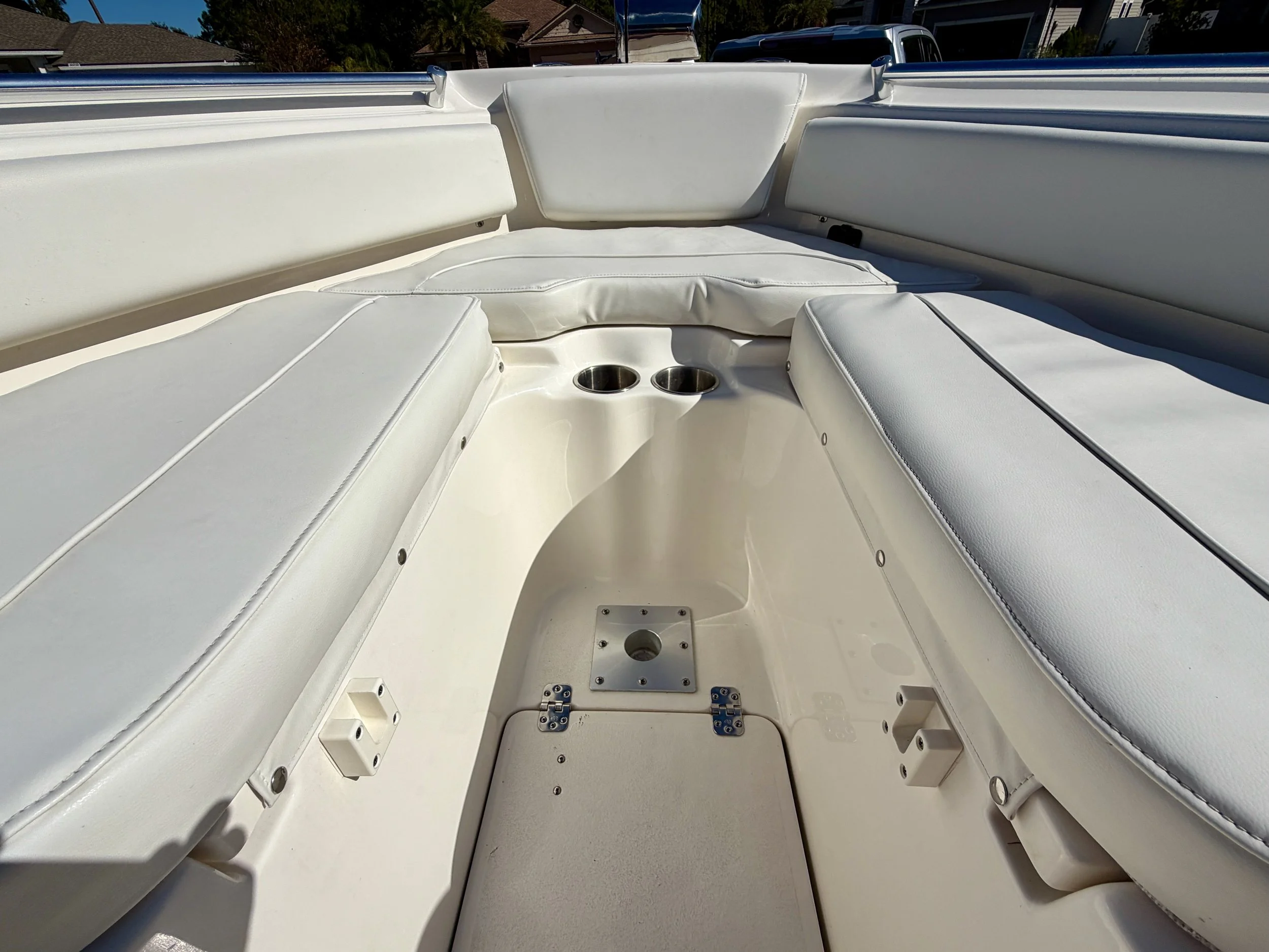 Interior of a white boat with cushioned seating, cup holders, and hardware fixtures.