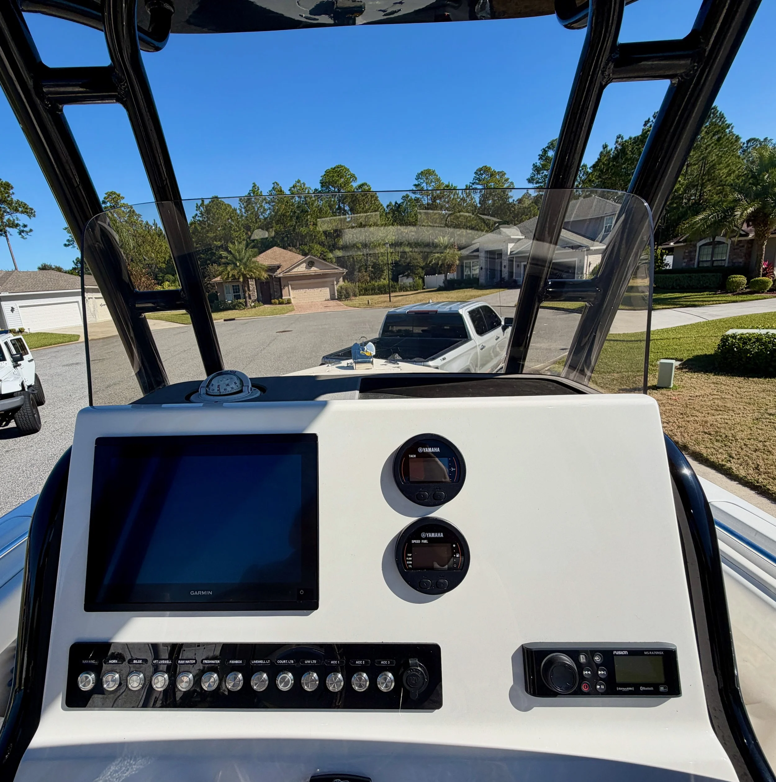 View from the cockpit of a boat showing navigation and control instruments, with a residential neighborhood and parked vehicles visible through the windshield.