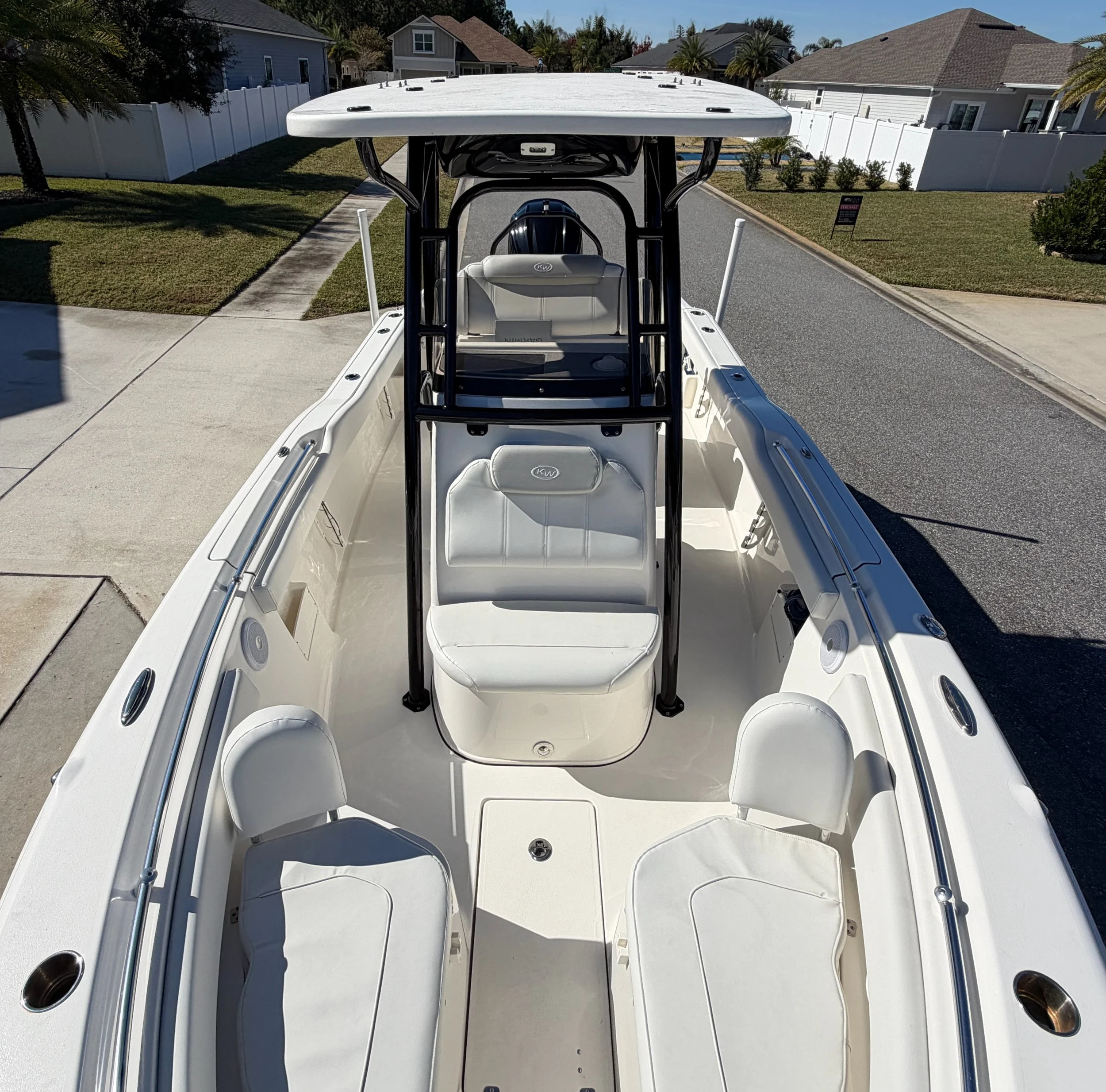 Front view of a white boat with four seats and a black T-top, parked on a residential street.