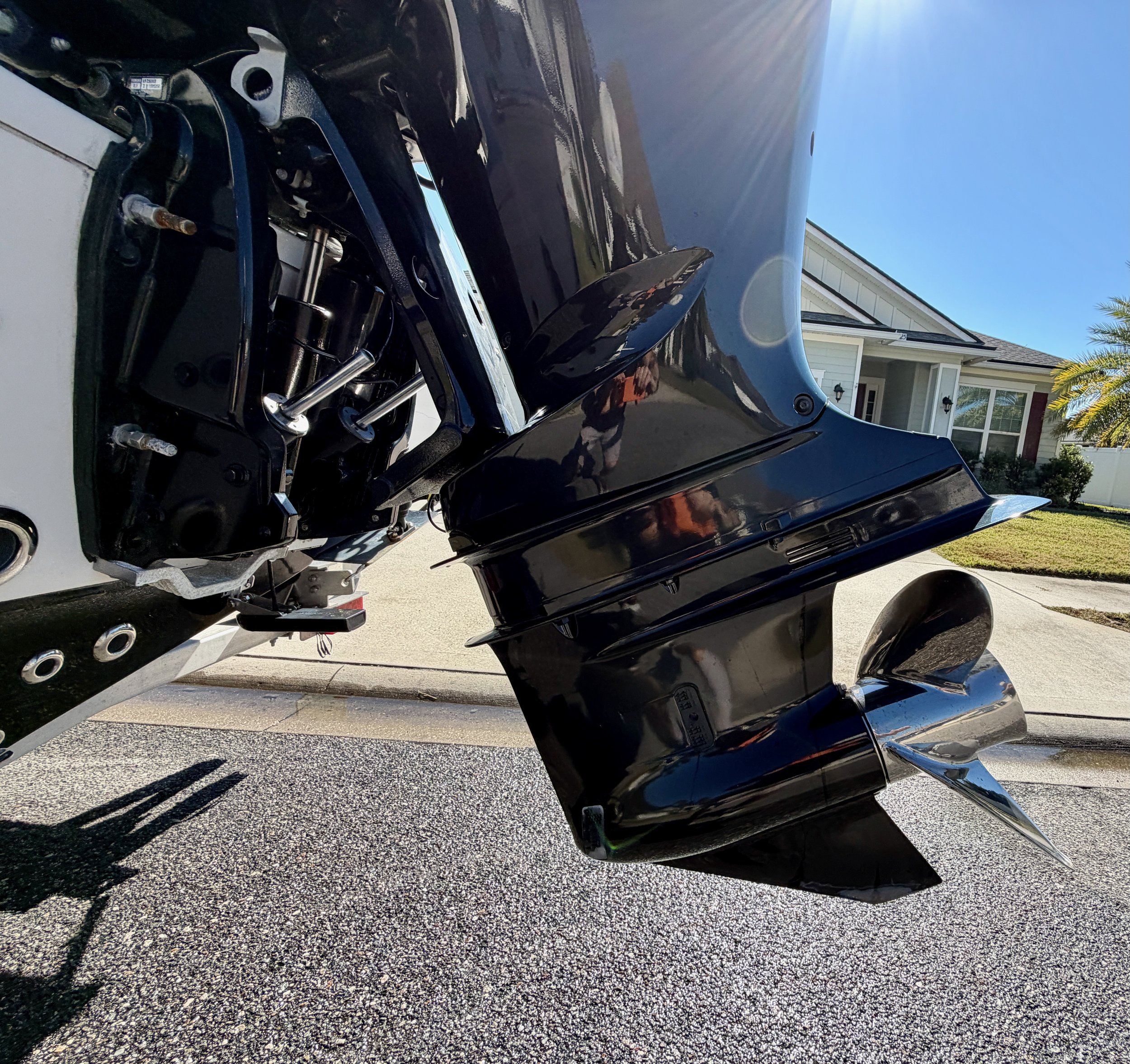 Close-up of a boat's outboard motor with a black cover on a residential driveway during sunny weather.