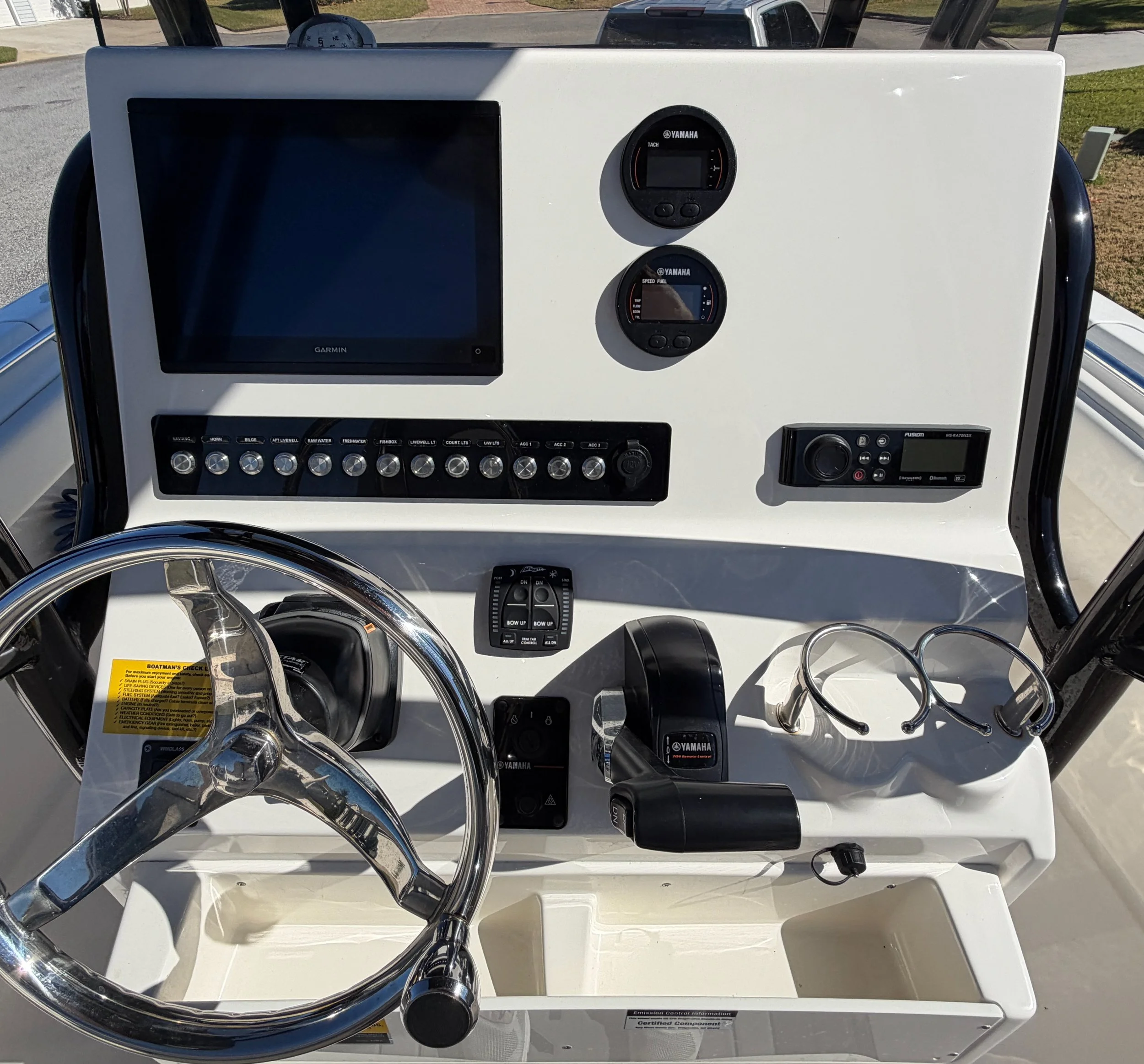 The image shows the helm of a boat with various navigational and control instruments, including a large screen, two round Yamaha gauges, switches, a radio, and a steering wheel.
