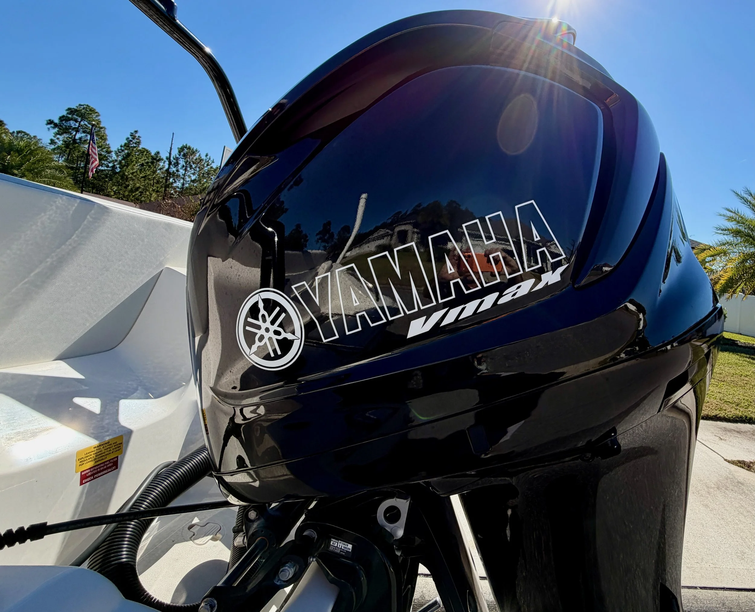 A close-up of a Yamaha Vmax outboard motor attached to a boat, with clear blue sky and some trees in the background.