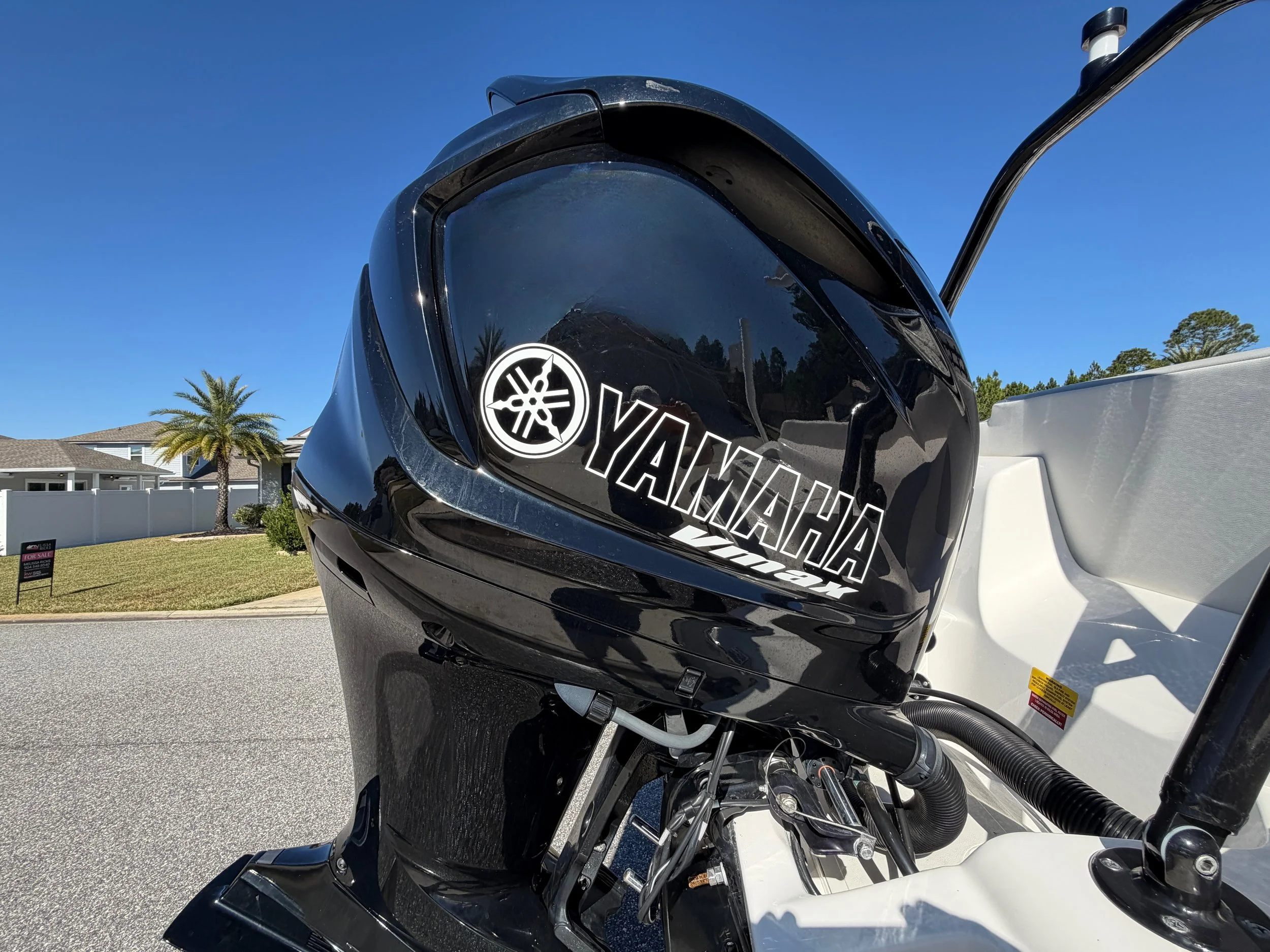 Close-up of a black Yamaha outboard motor mounted on a boat, with a clear blue sky and residential houses with palm trees in the background.