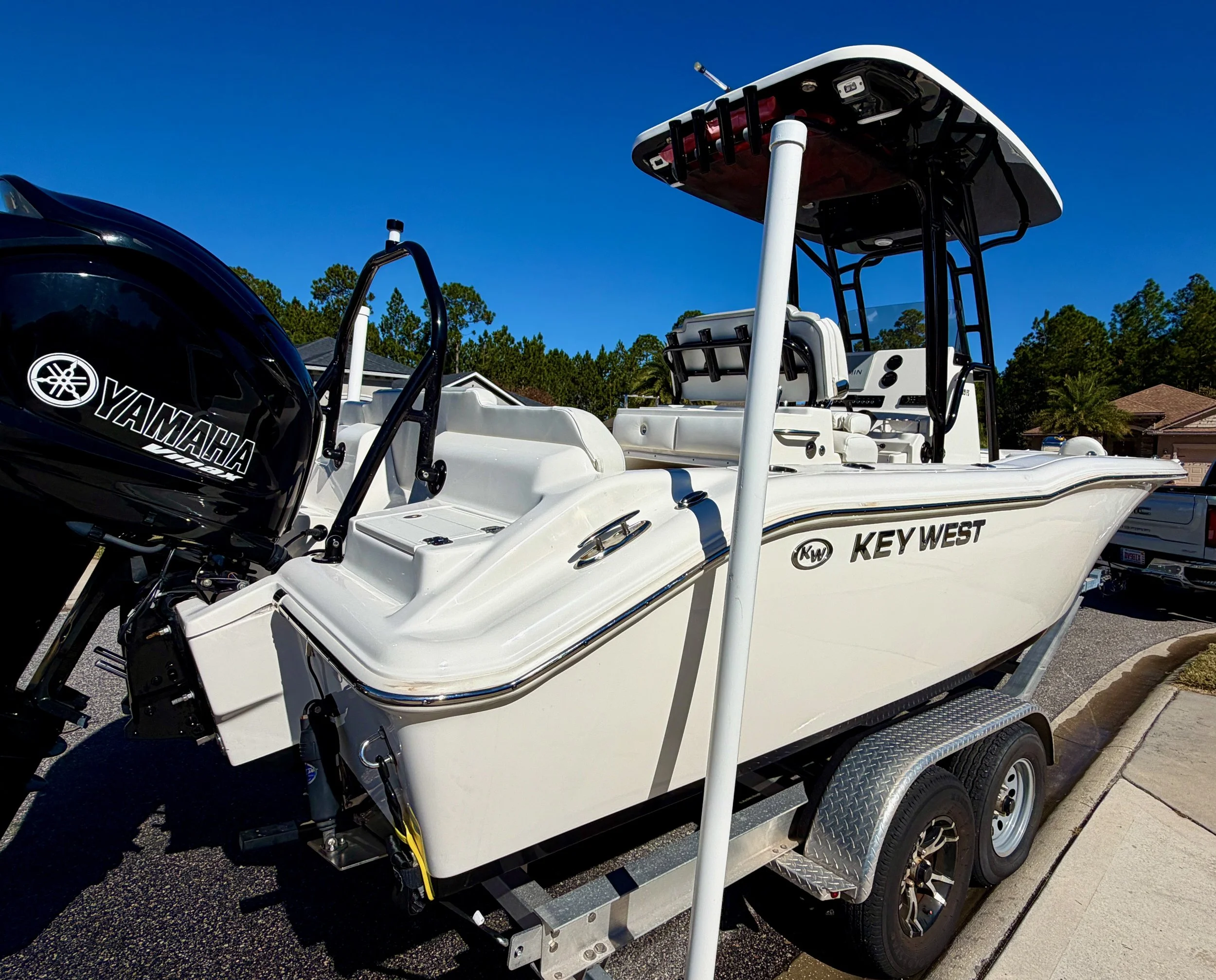 A white Key West boat on a trailer with a Yamaha outboard motor, parked on a residential street under a blue sky with trees and houses in the background.