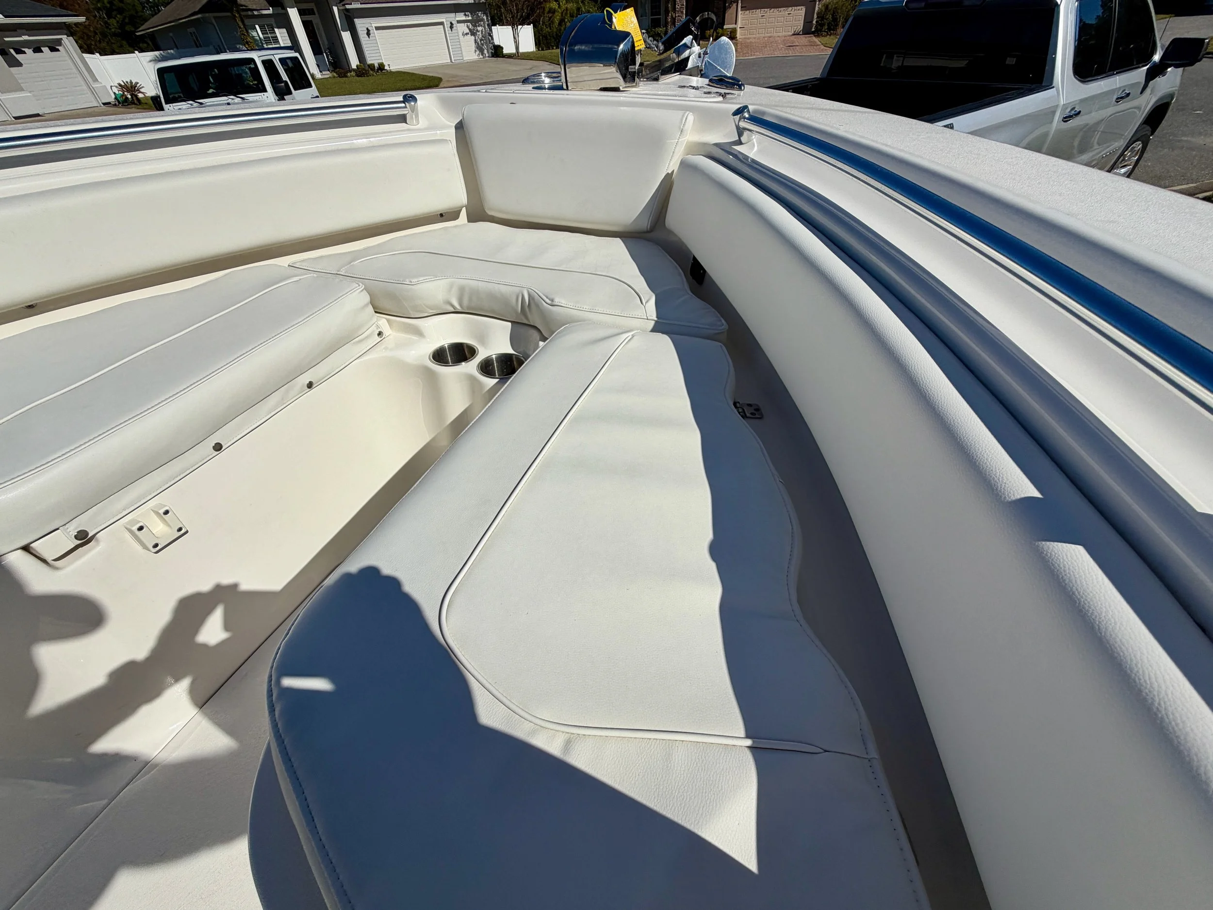 Close-up of the white cushioned seating and drink holders on a boat's deck, with parked cars and residential houses visible in the background.