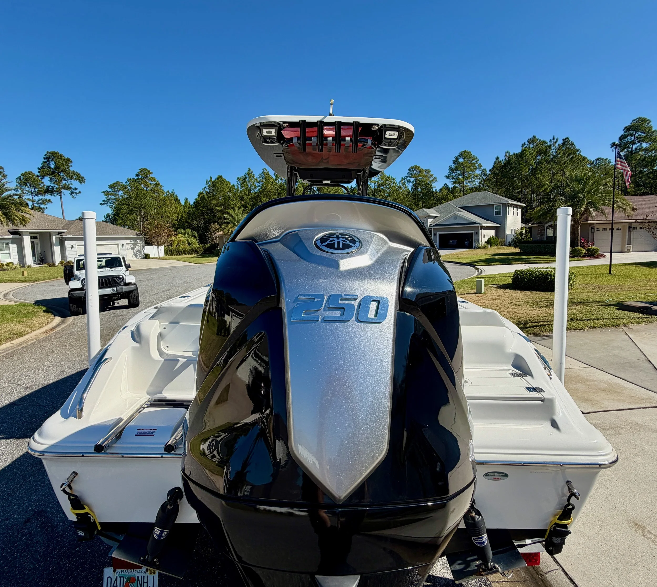 A boat with a Yamaha 250 horsepower outboard motor parked in a driveway in a suburban neighborhood, with houses and a clear blue sky in the background.