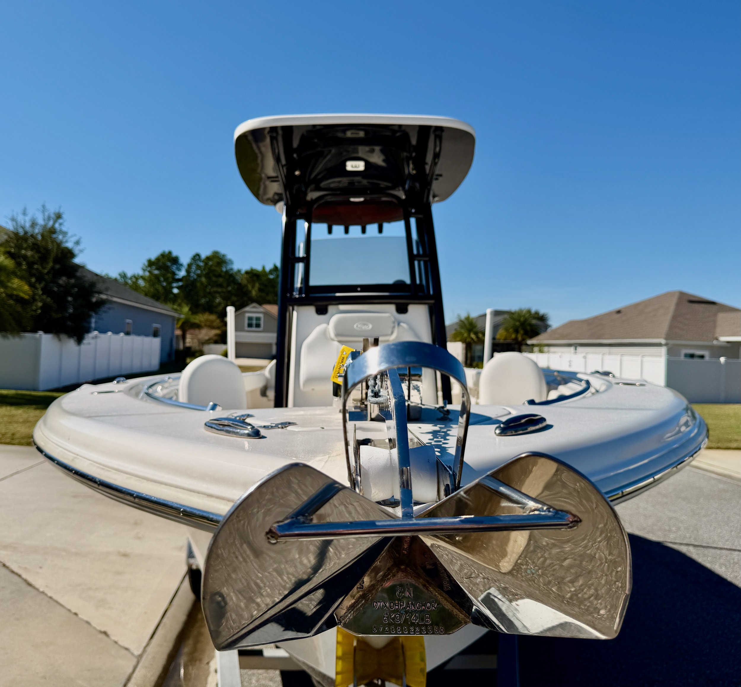 Front view of a white boat with a metal propeller, parked on a driveway under a clear blue sky, with houses and trees in the background.