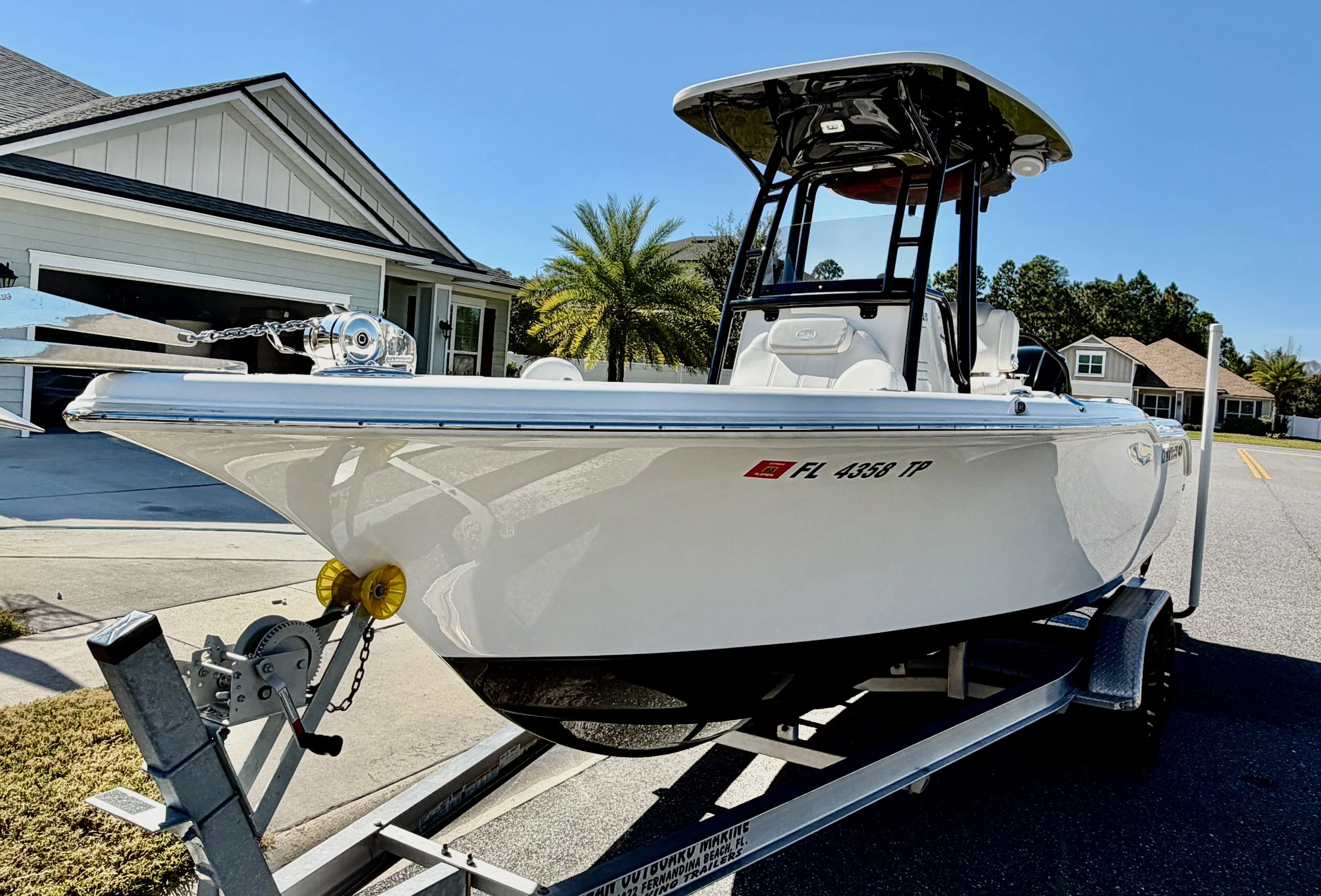 A white speedboat on a trailer in a residential neighborhood on a sunny day.