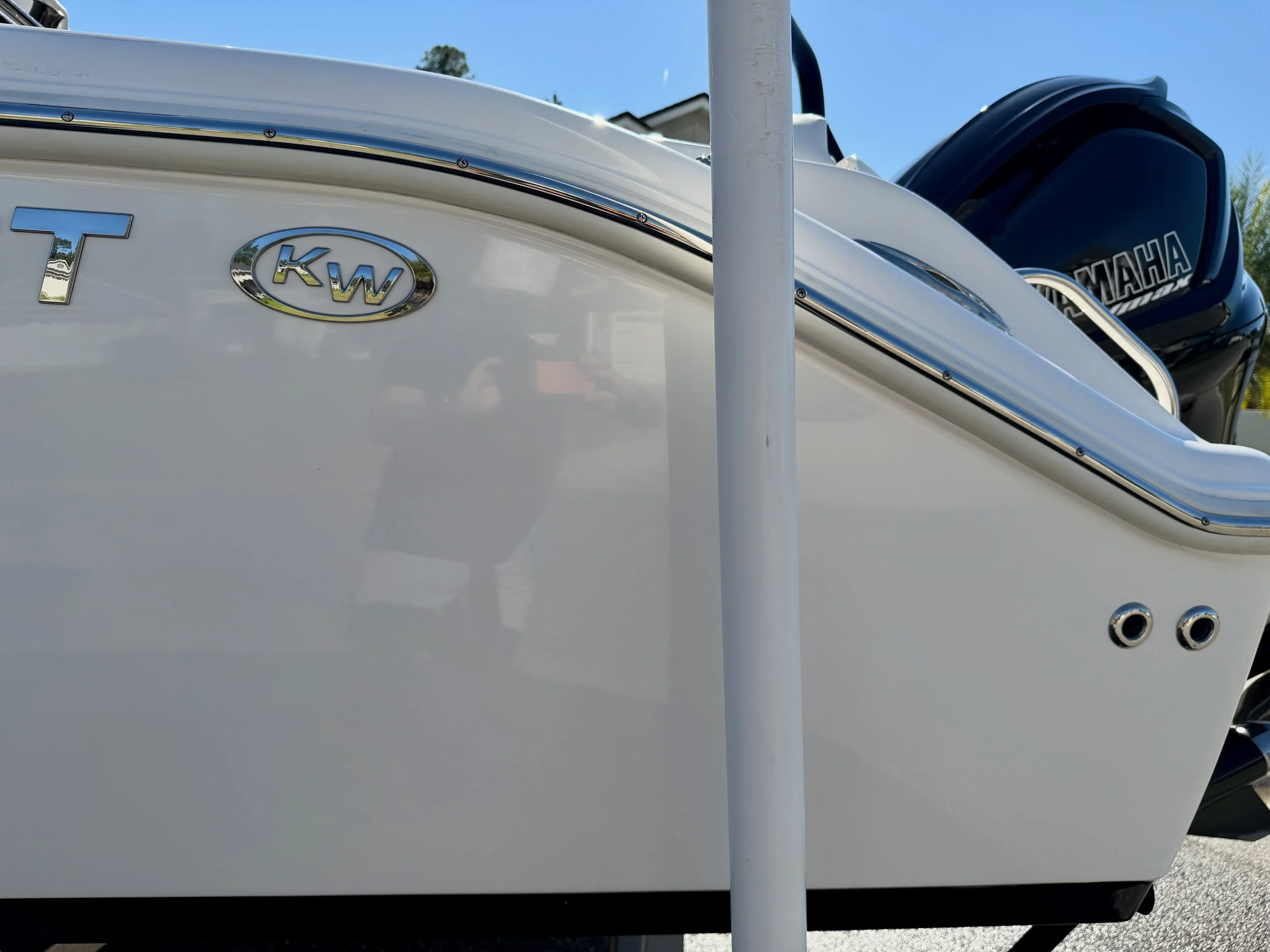 Close-up of a white boat with a Yamaha outboard motor and a KW logo badge on the side, with a pole and a building in the background.