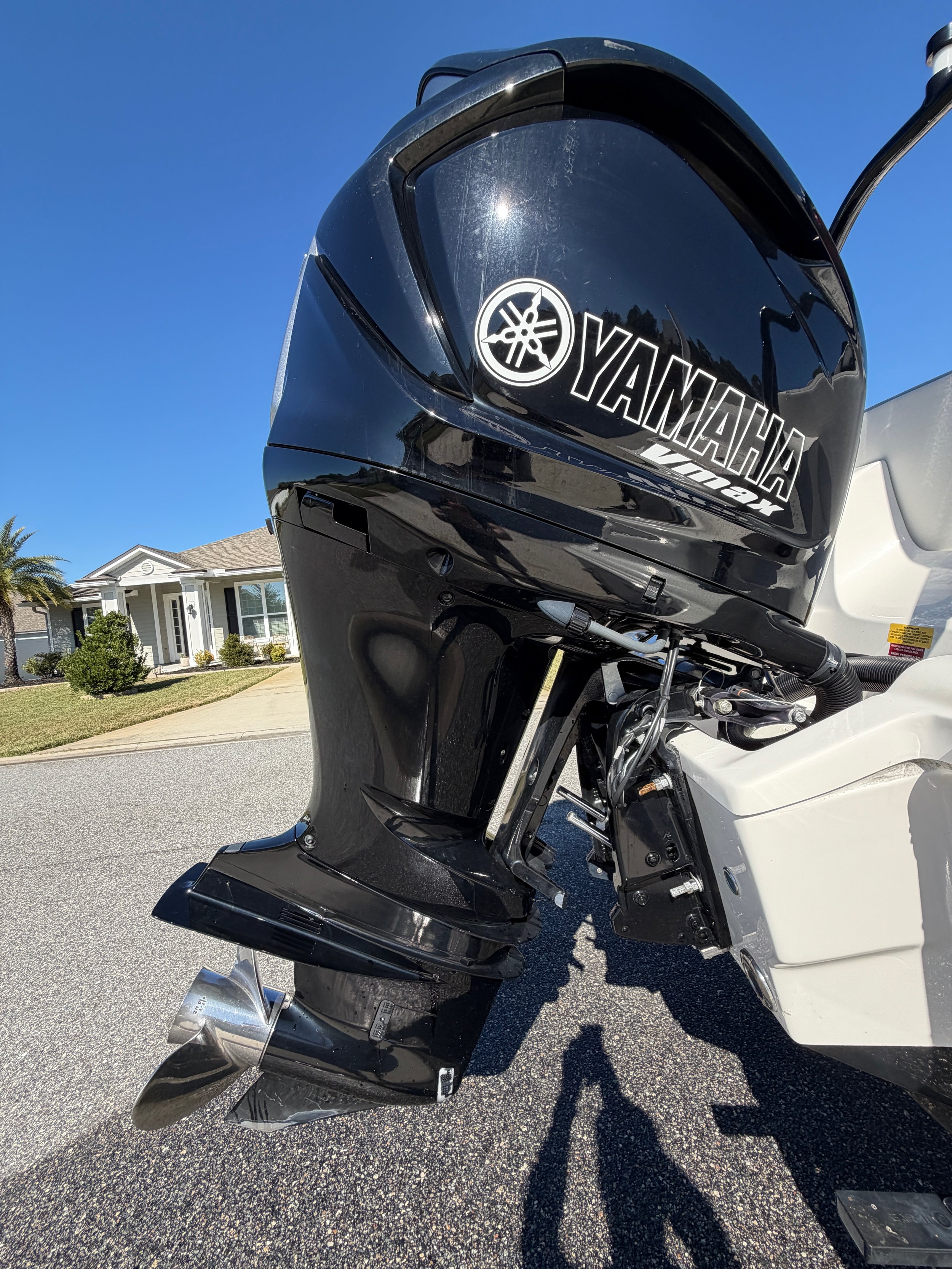 Close-up of a Yamaha outboard motor attached to a boat, with a house and clear blue sky in the background.