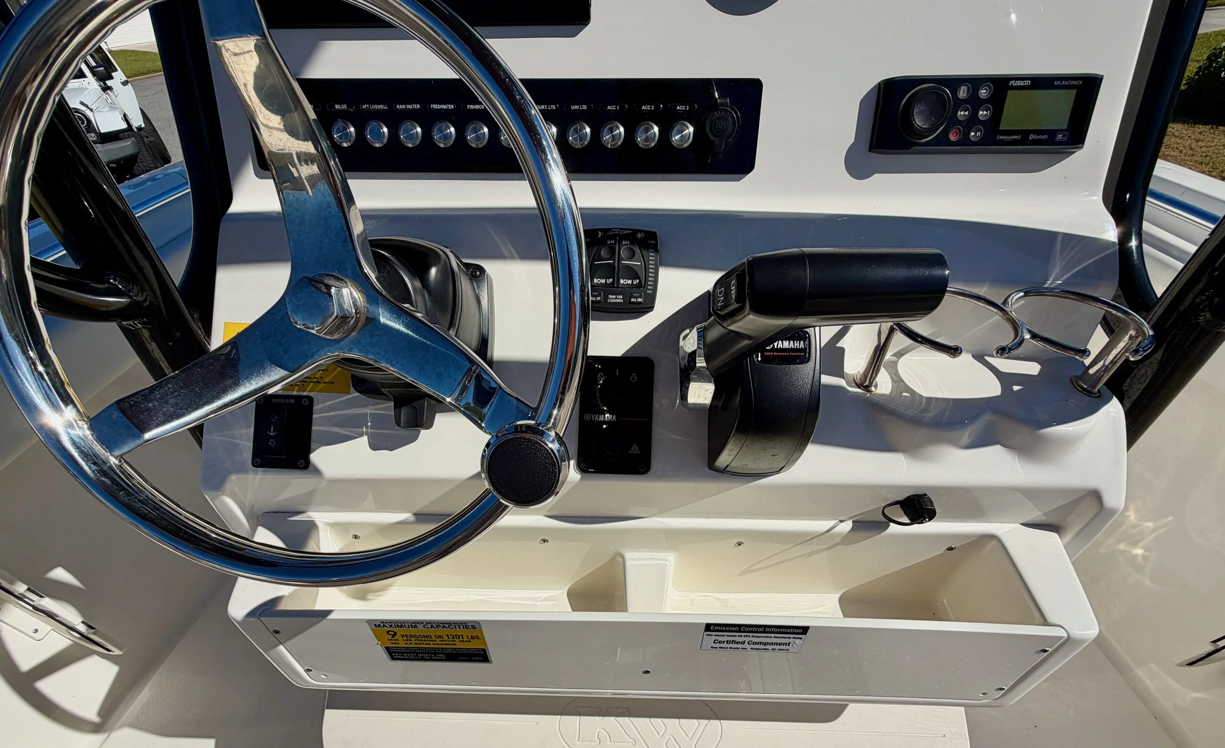 The dashboard of a boat showing a steering wheel, throttle, control switches, and electronic displays.