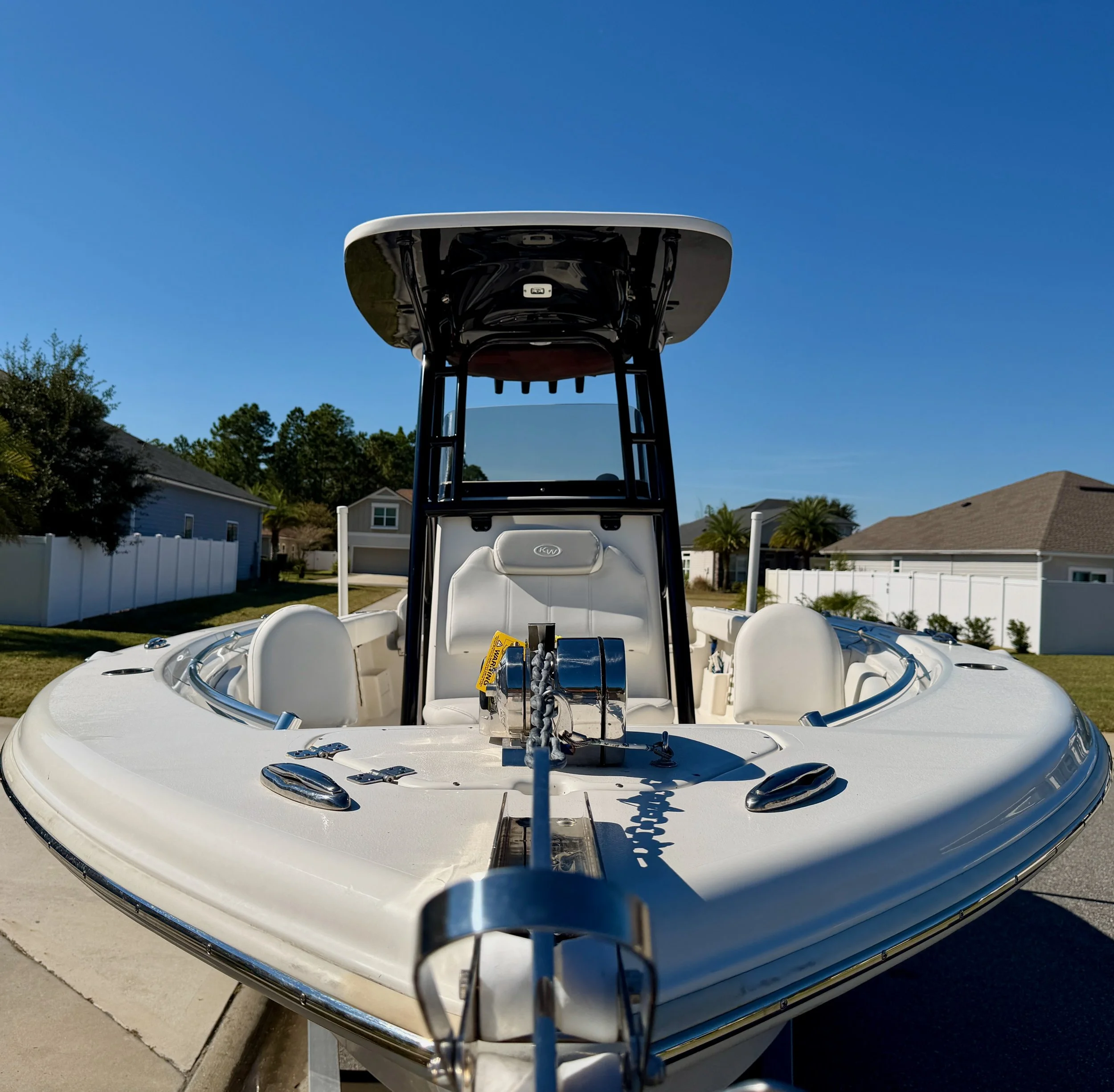 Front view of a white motorboat parked on a driveway with houses and trees in the background under a clear blue sky.