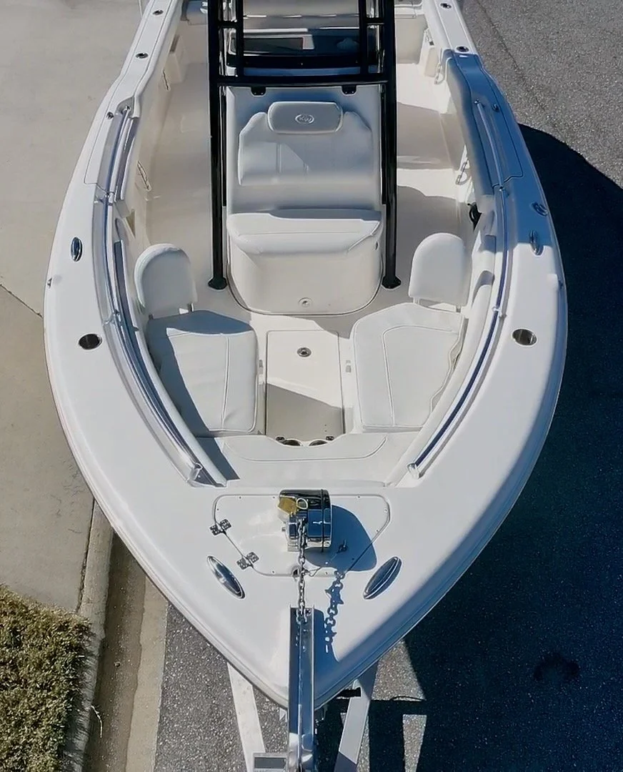 A white boat with a bow and seating area, parked on a trailer on the pavement.