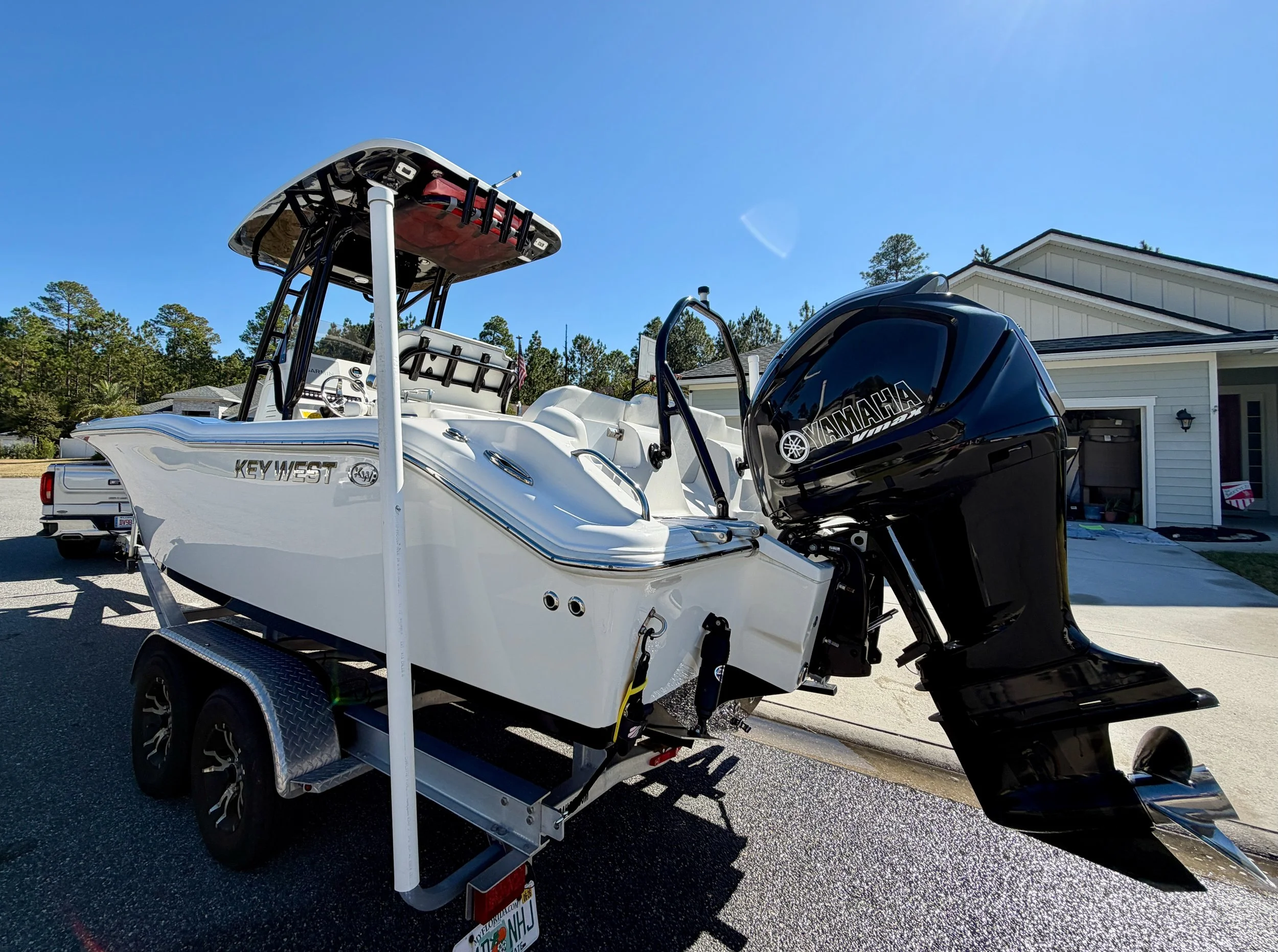 White Key West boat with a Yamaha outboard motor on a trailer parked in front of a house on a sunny day.