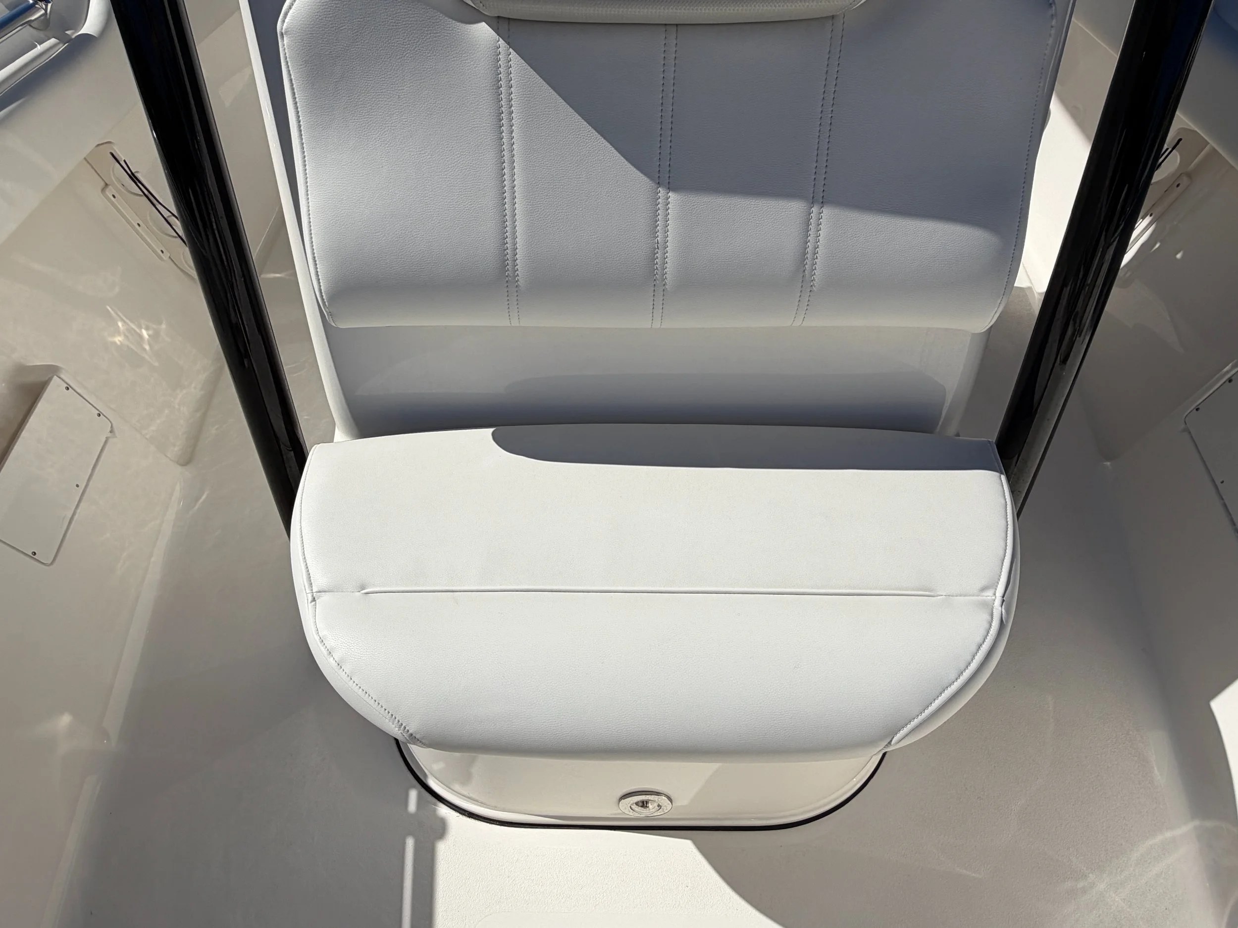 Close-up of a white cushioned boat seat with a backrest and a metal frame, painted black, with a shadow cast onto the seat from sunlight.