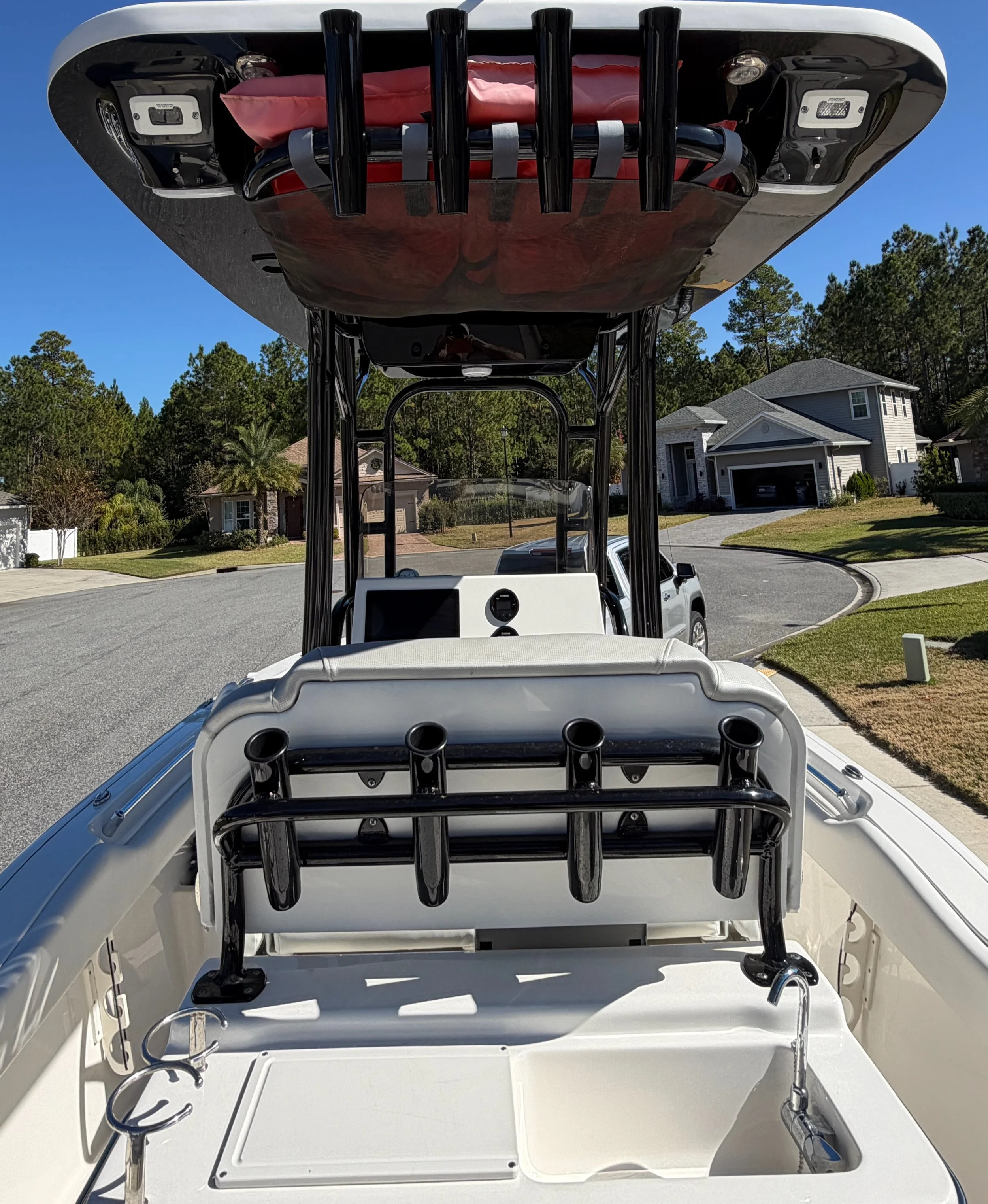 View from the back of a white boat with fishing rod holders and a small sink, parked on a residential street under a clear blue sky.