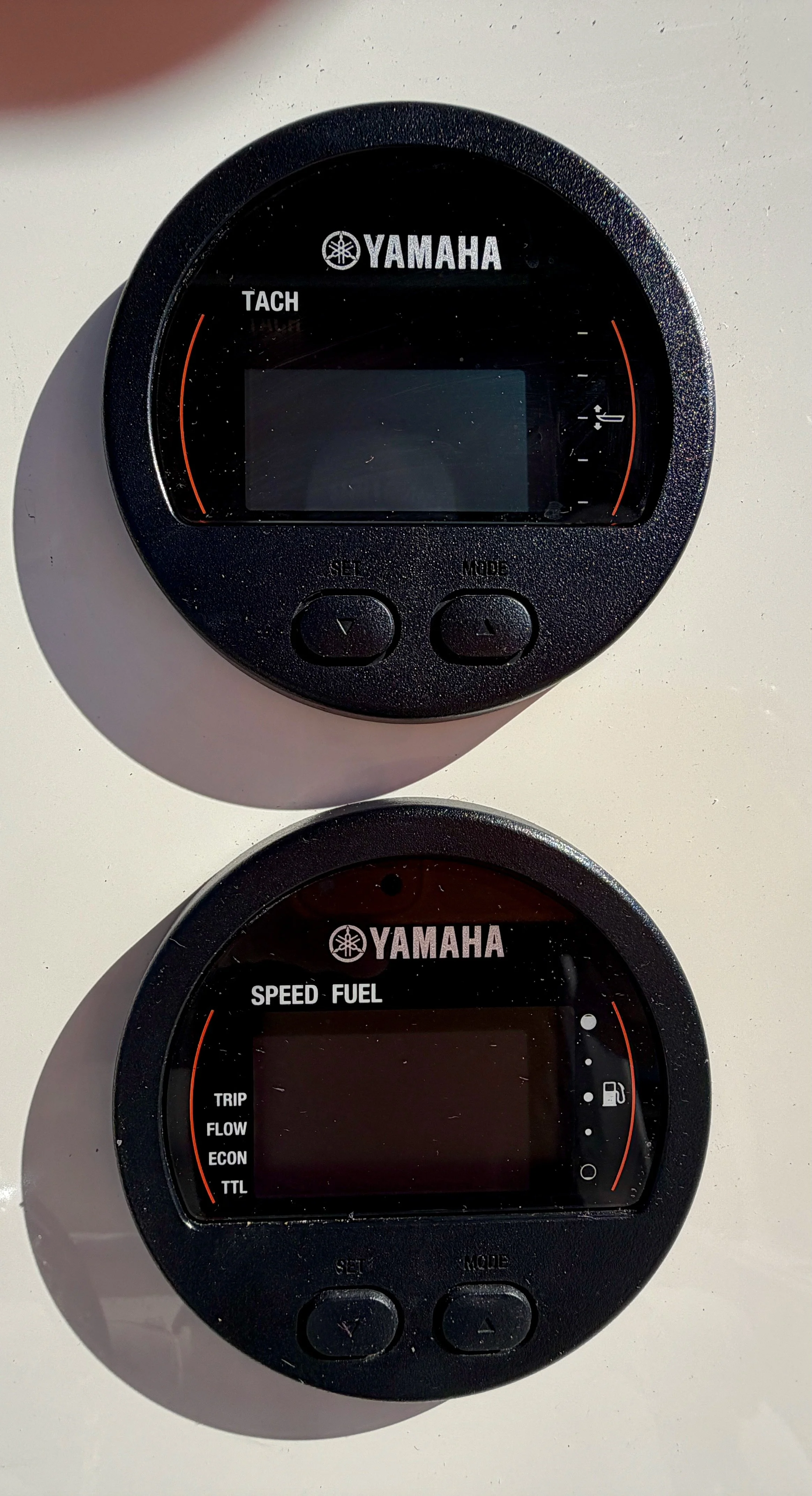 Two Yamaha digital gauges, one displaying tachometer and the other showing speed and fuel level, mounted on a white surface.