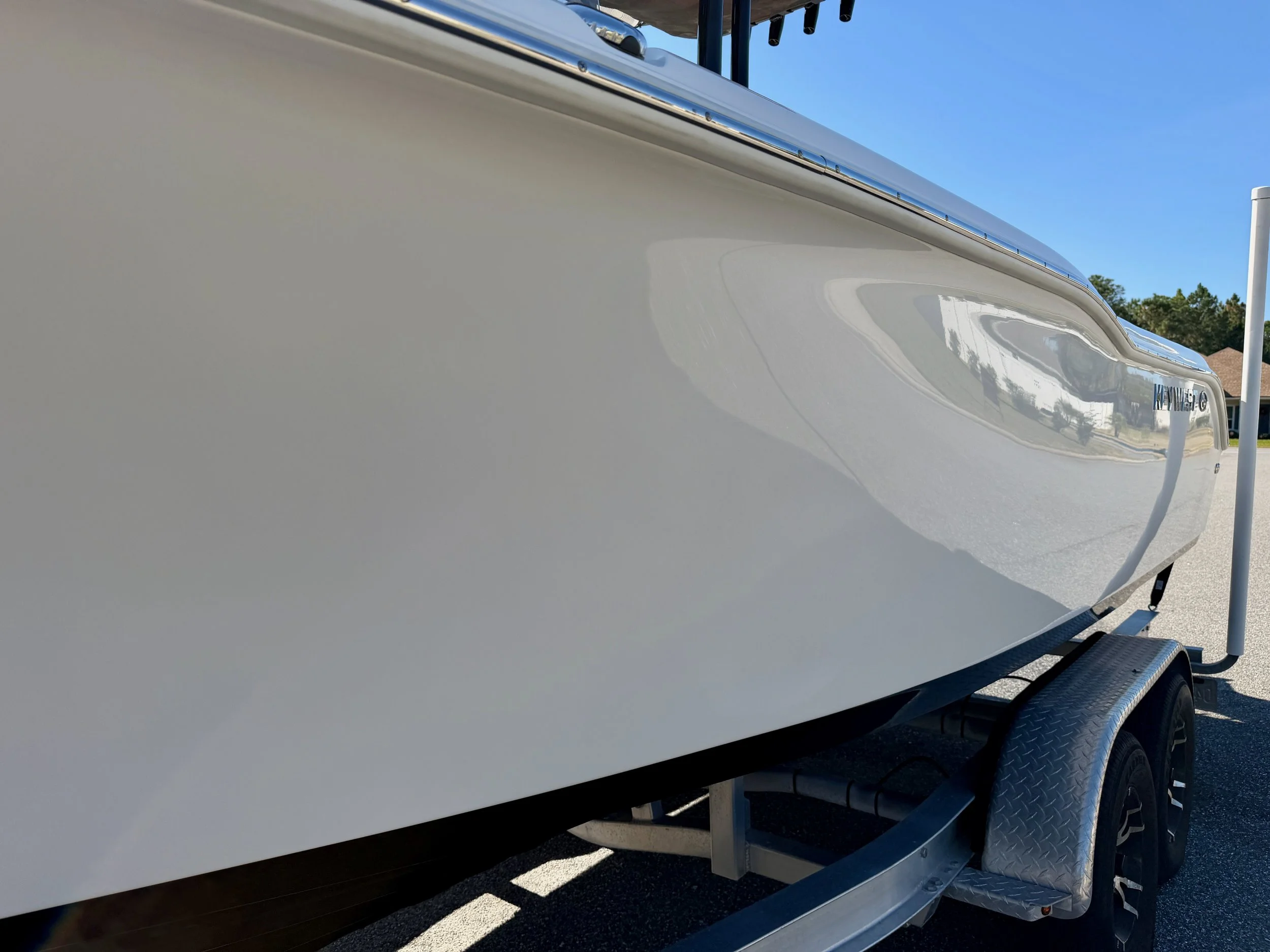 White boat on a trailer parked on a paved driveway under a clear blue sky.
