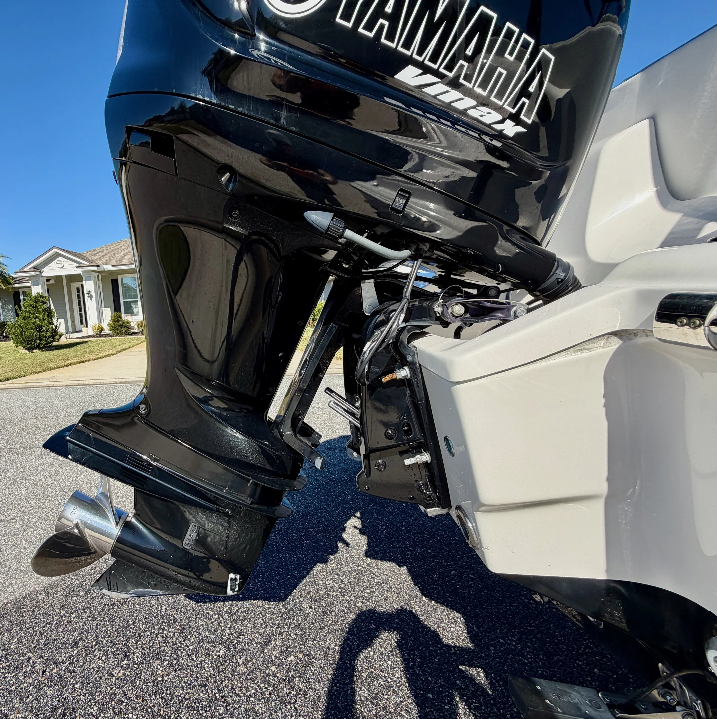 Close-up view of a boat motor on a white boat, with a house and a clear blue sky in the background.