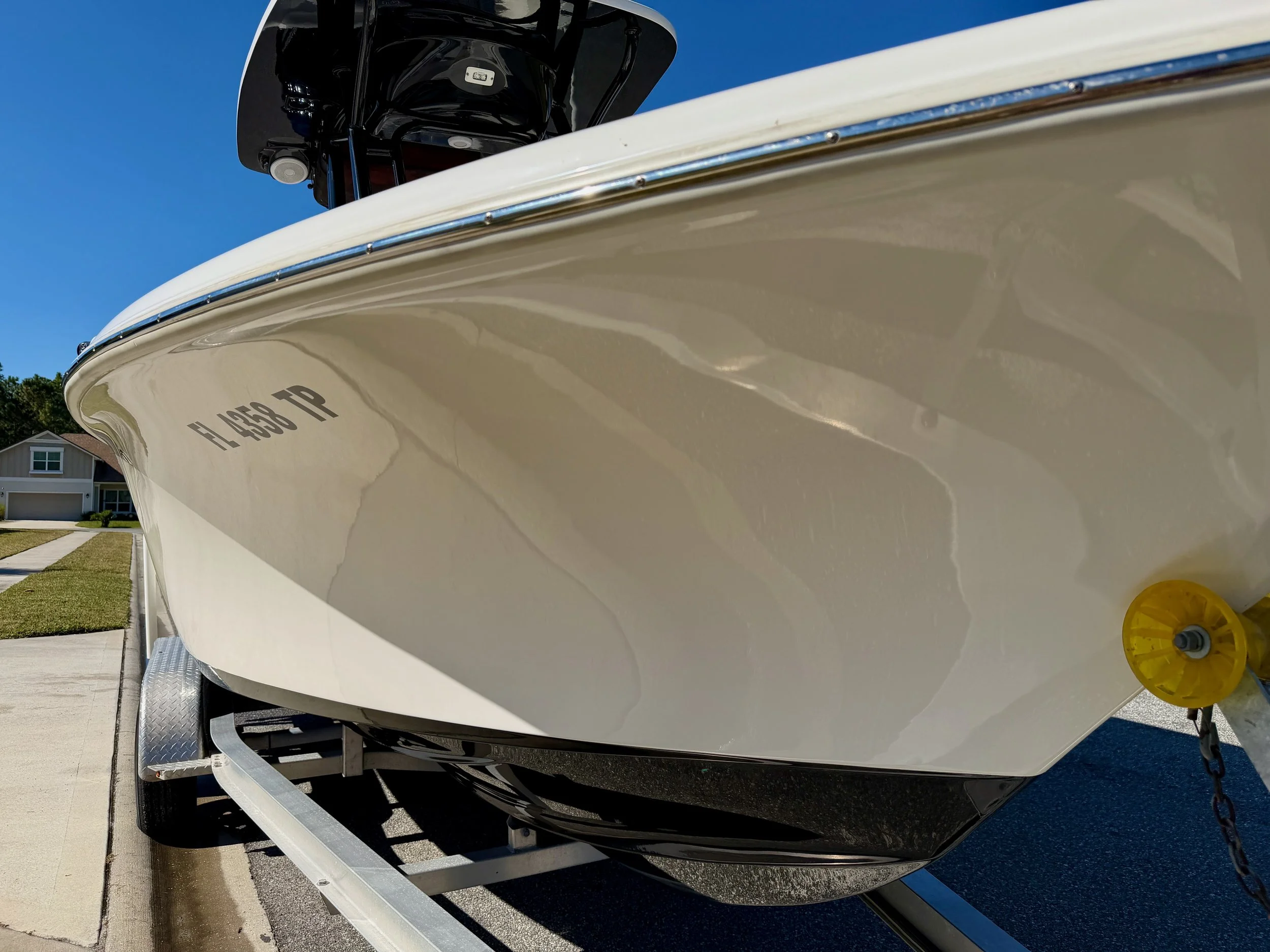 Close-up of the bow of a white boat on a trailer, with the boat's registration number 'FL 4538 TP' visible, parked on a residential street under a clear blue sky.