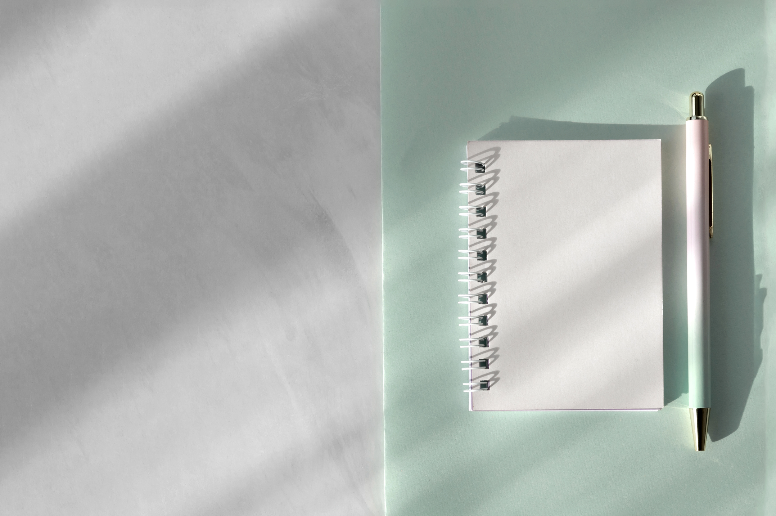 A white spiral notebook with a blank cover, a pastel pink and gold pen, and a light green sheet of paper, arranged on a flat surface with shadows. What’s the difference between a logo and a brand?