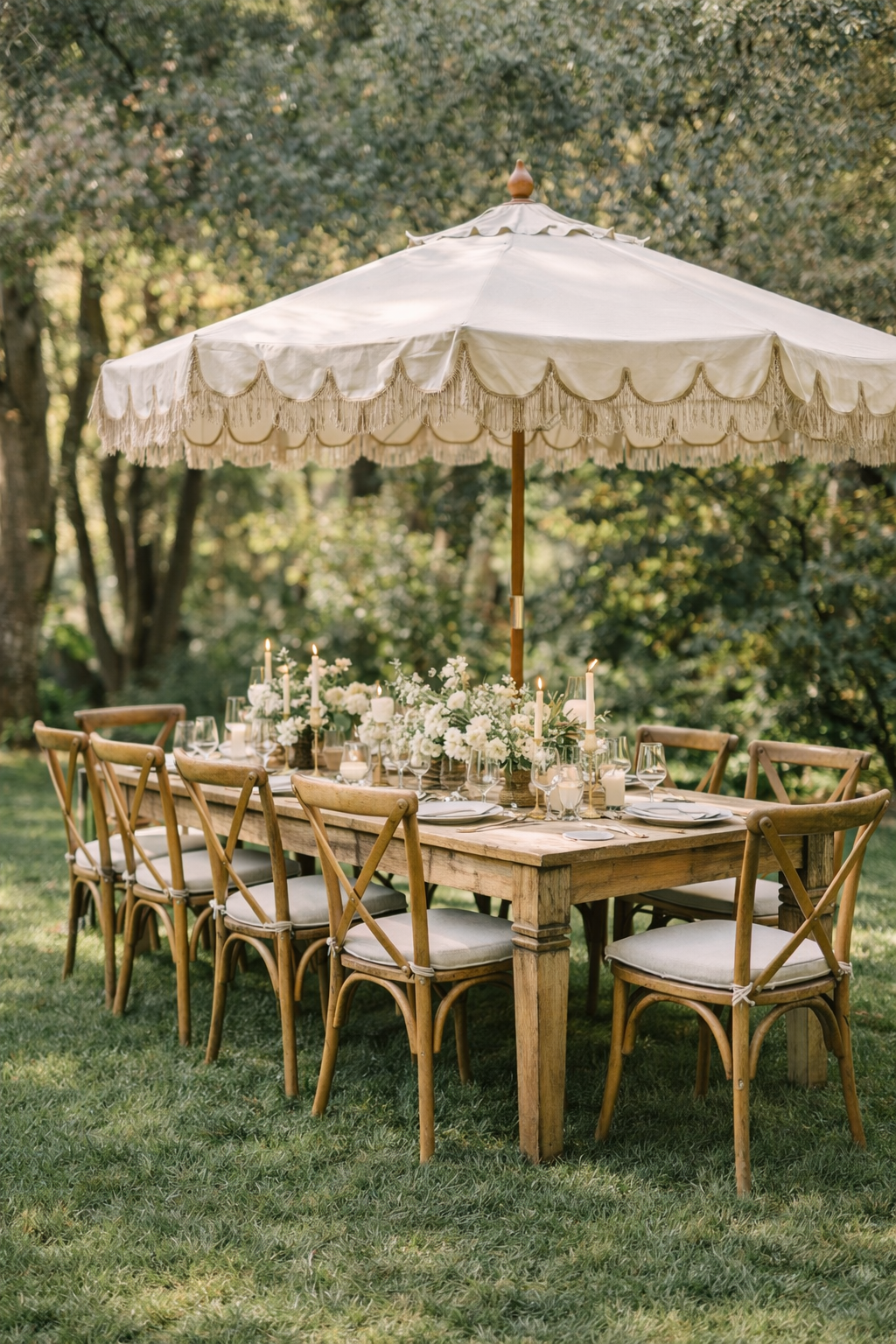 An outdoor dining table set for a formal event with a large white umbrella, candles, white flowers, tableware, and wooden chairs, in a lush green garden. How do I style a small event space?