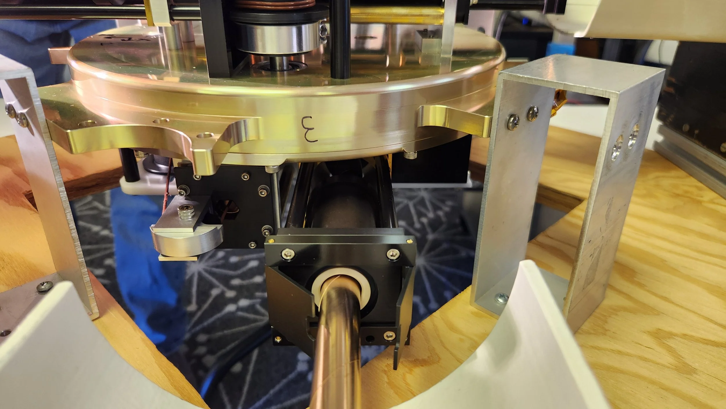 Close-up view of a mechanical or engineering component with metal parts, screws, and a black cylindrical element, mounted on a wooden surface.