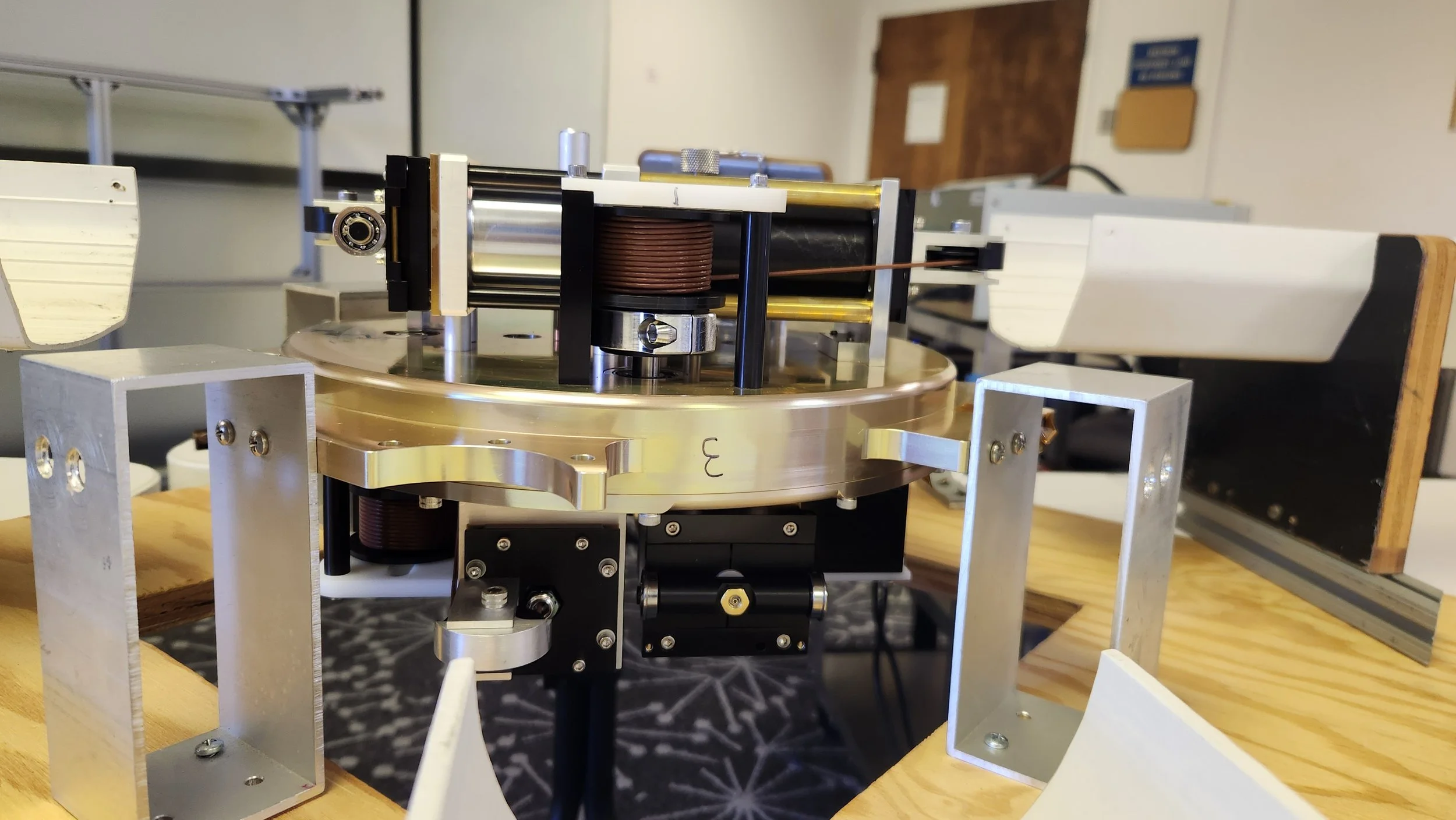 A scientific experimental setup including rotating circular platform with mechanical and electronic components, mounted on a wooden table.