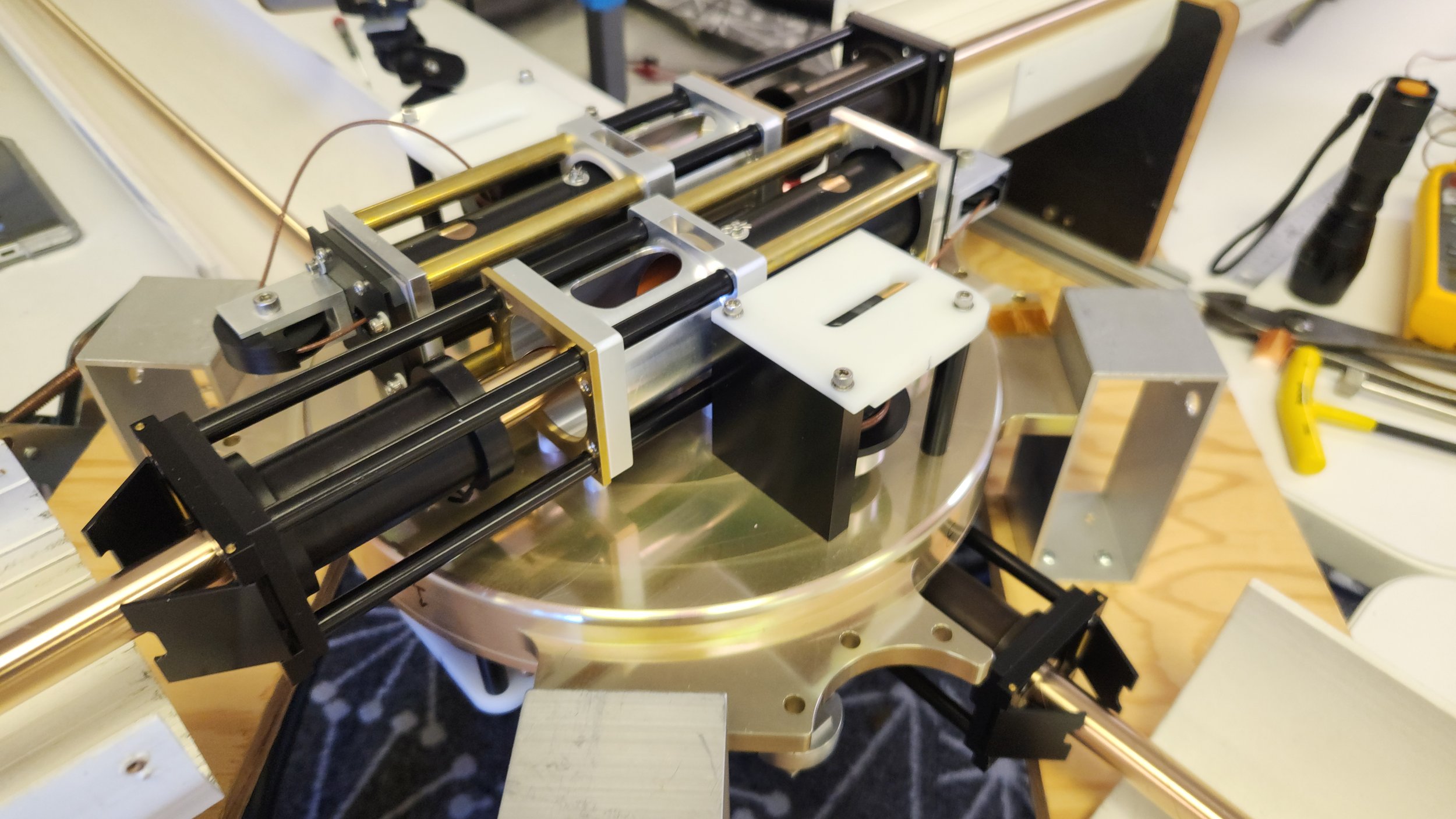 Close-up of a mechanical device with metal rods, sliders, and electronic components on a workbench.
