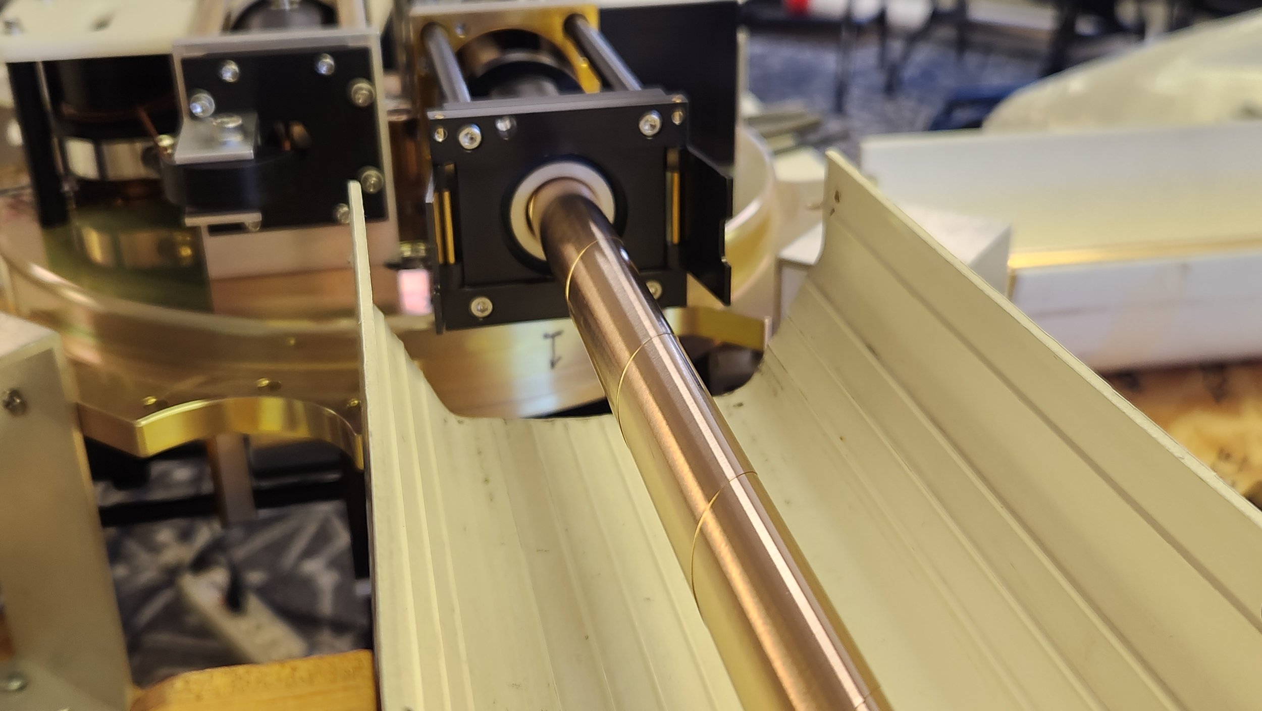 Close-up of a metallic shaft attached to a black motor housing with yellow accents, mounted on an aluminum frame with grooves, possibly part of a robotic or mechanical system.