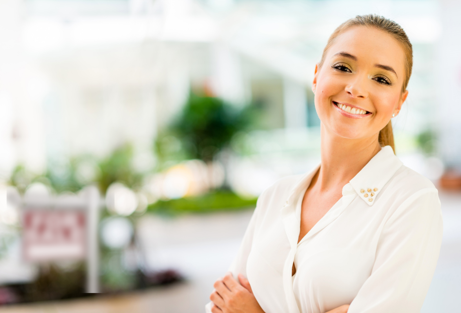A well put together, professionally dressed woman in front of a blurry background with a nice home with a for sale sign in the yard