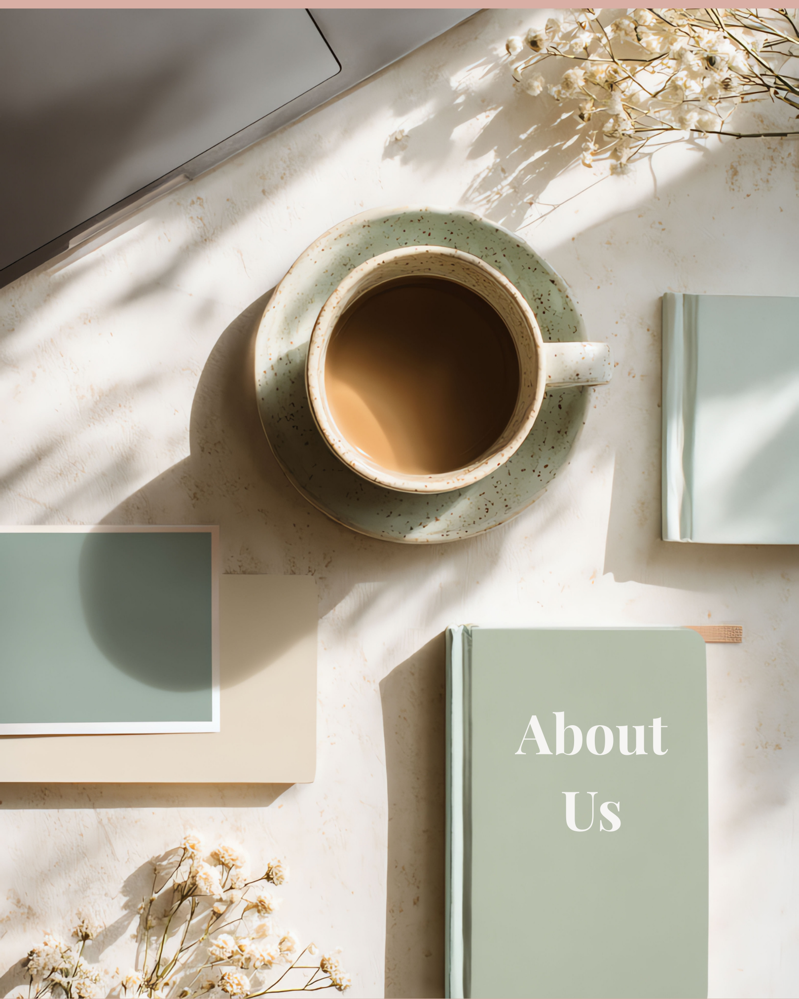 A flat-lay of a coffee cup, surrounded by a laptop, stationary, flowers and a book that says "about us"
