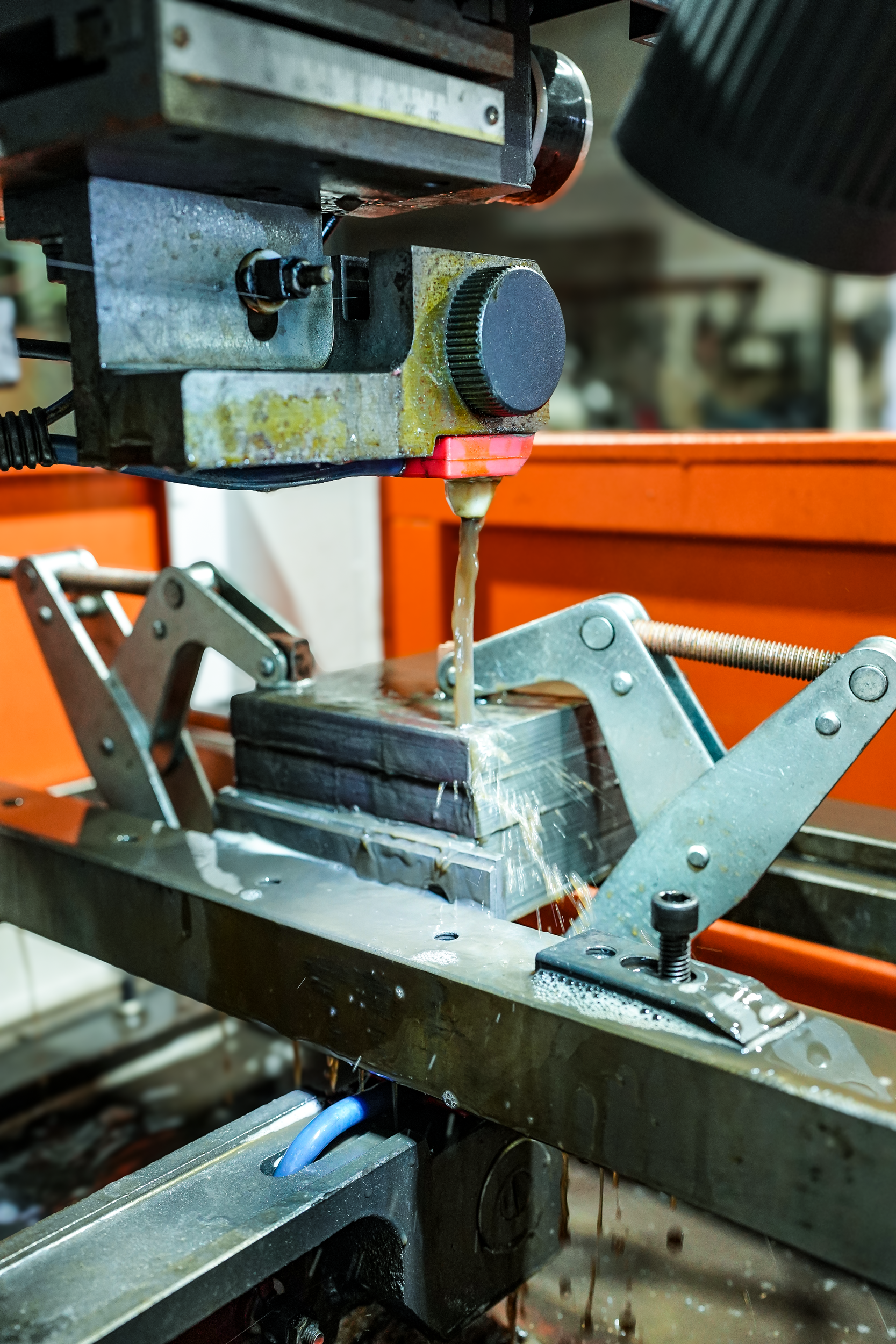 Close-up of a metal machining or drilling machine with some liquid or coolant leaking or dripping from it, situated on an industrial workbench.
