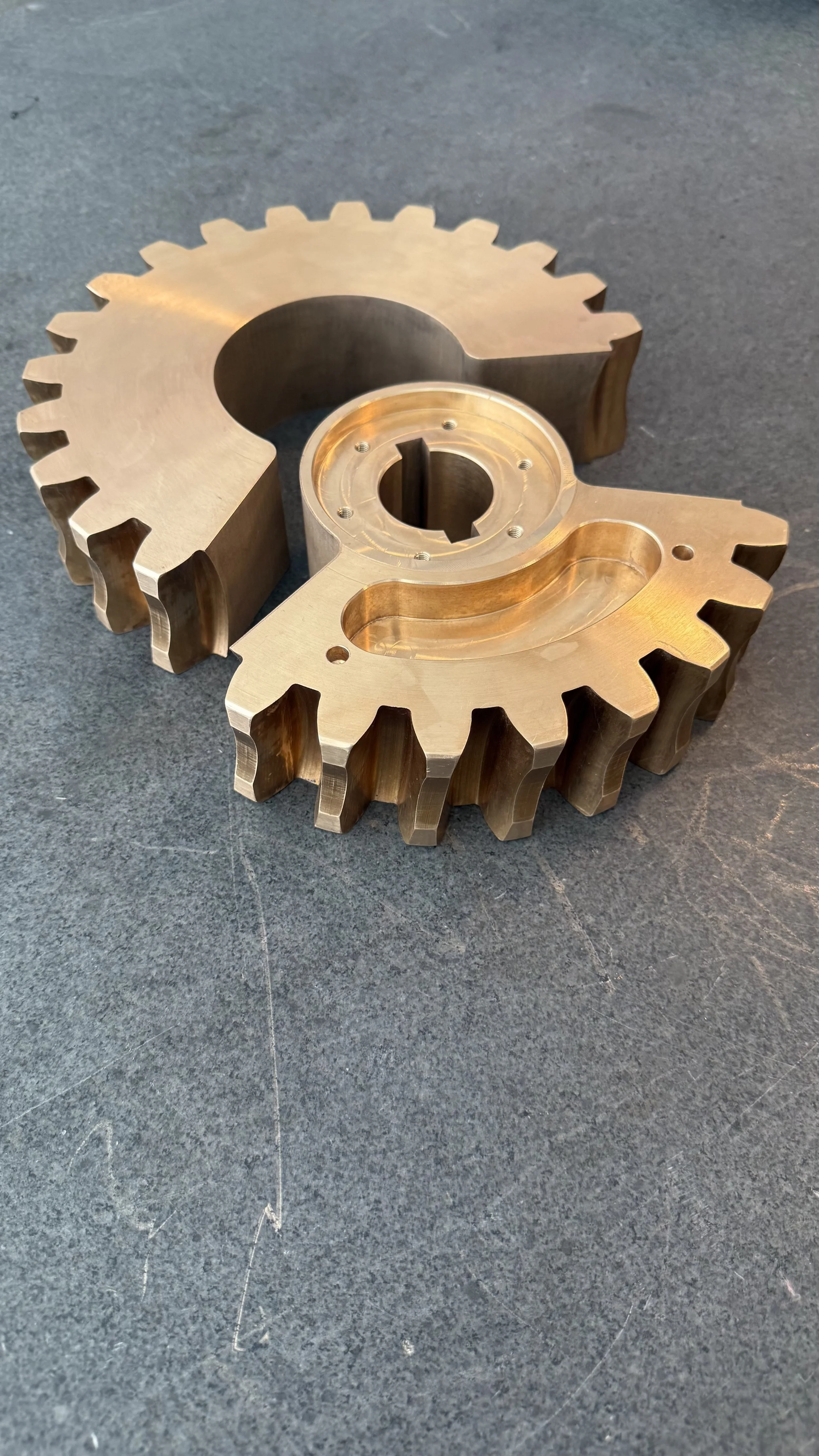 A close-up of a metallic gear component with interlocking teeth, placed on a textured dark surface.