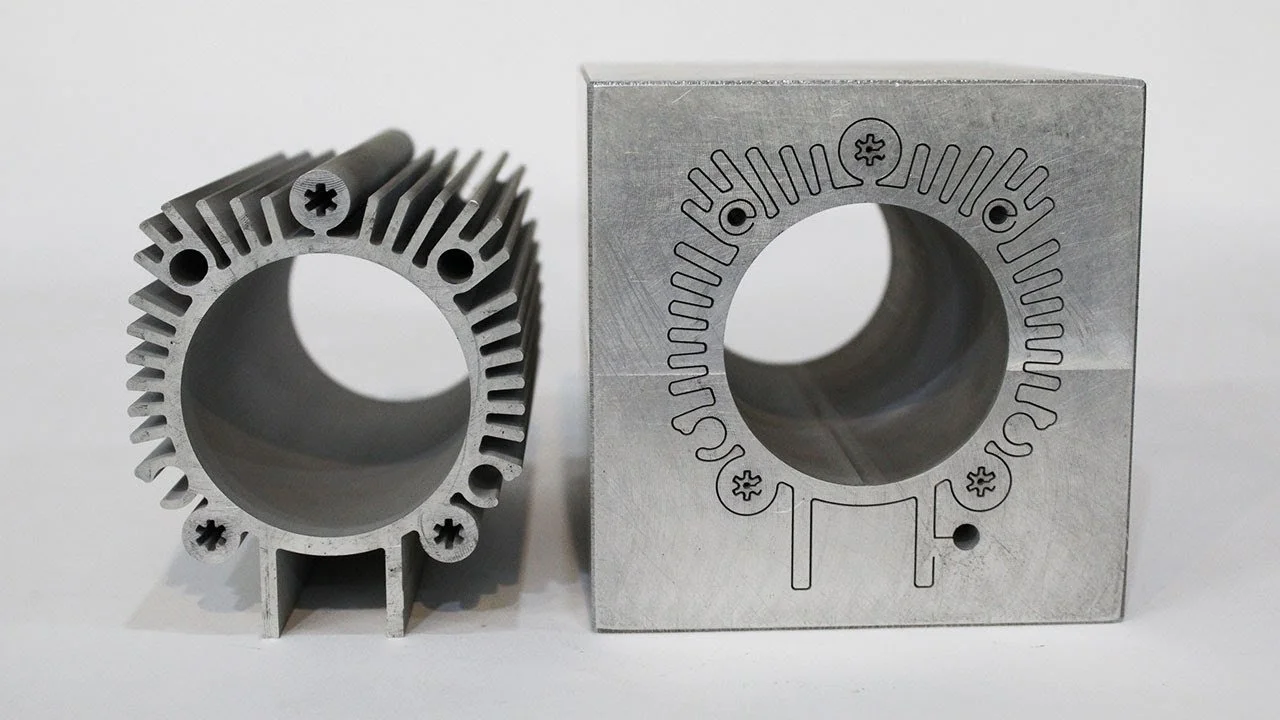 Two machined aluminum objects, one cylindrical with fins and the other a square block with a circular hole, both with engraved markings.