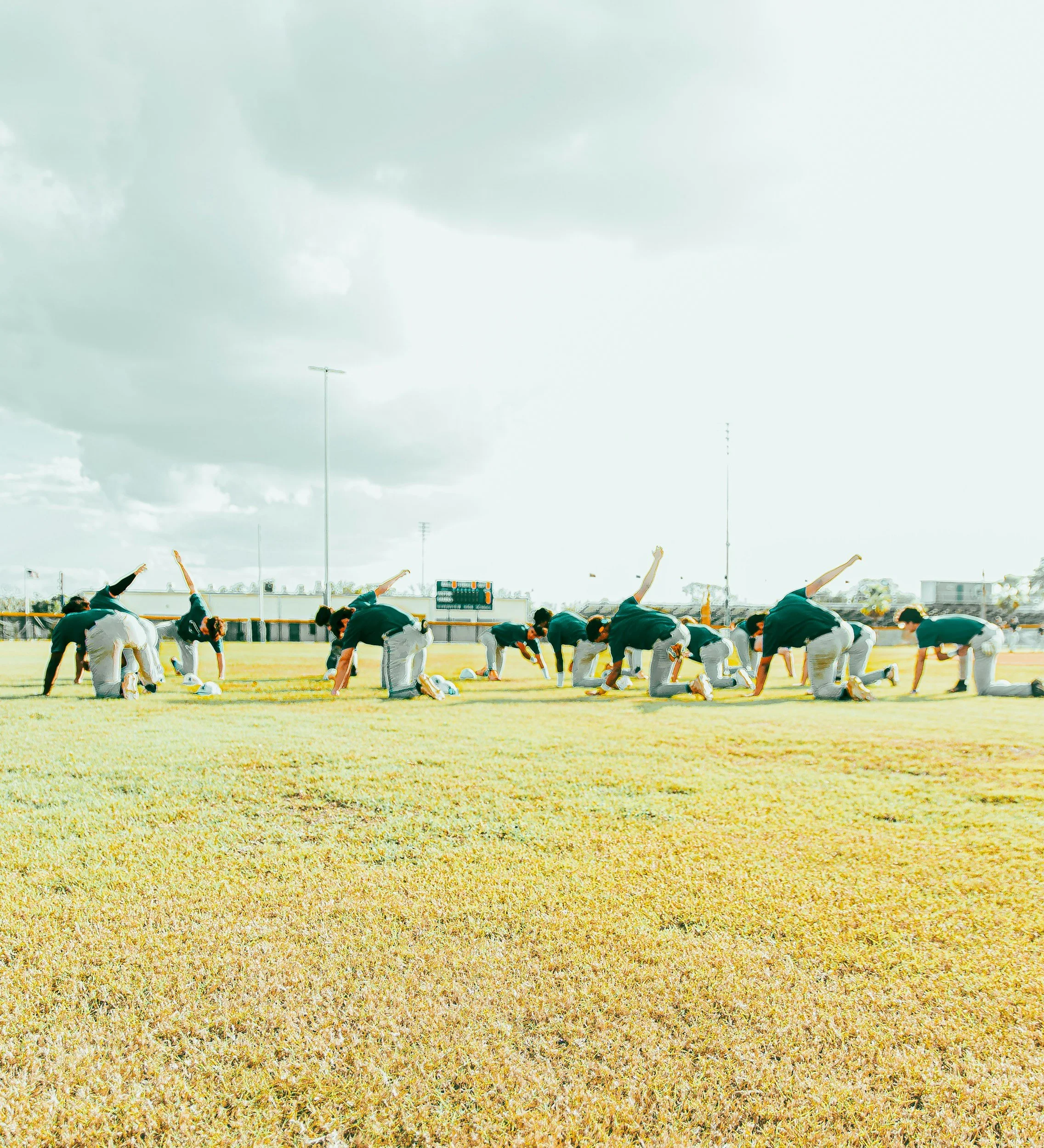 A baseball team practicing outdoors on a field on a cloudy day.