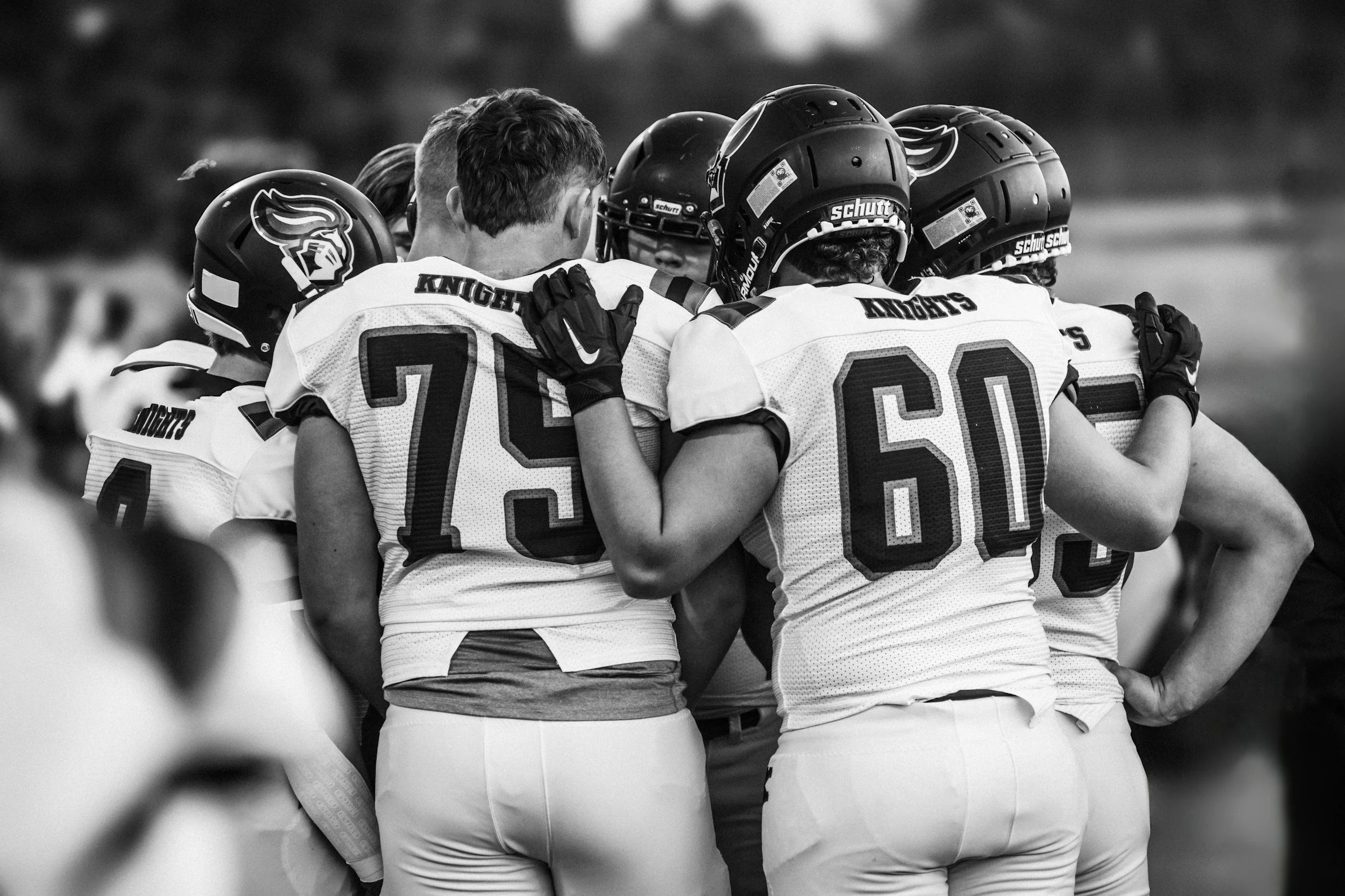 A group of football players, wearing helmets and jerseys, huddled together in a team huddle during a game or practice.