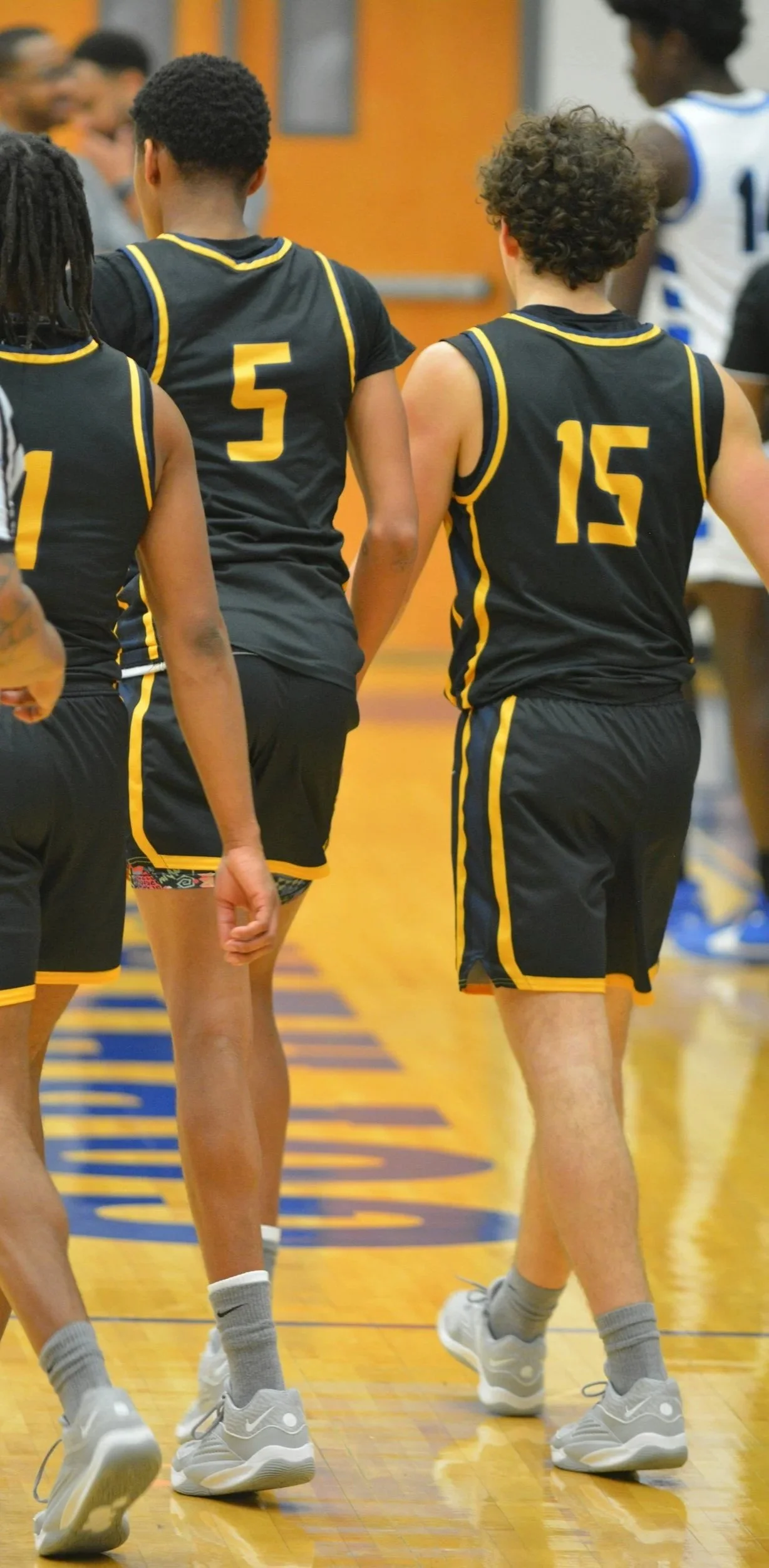 Basketball players in black and yellow uniforms walking on a gymnasium court.