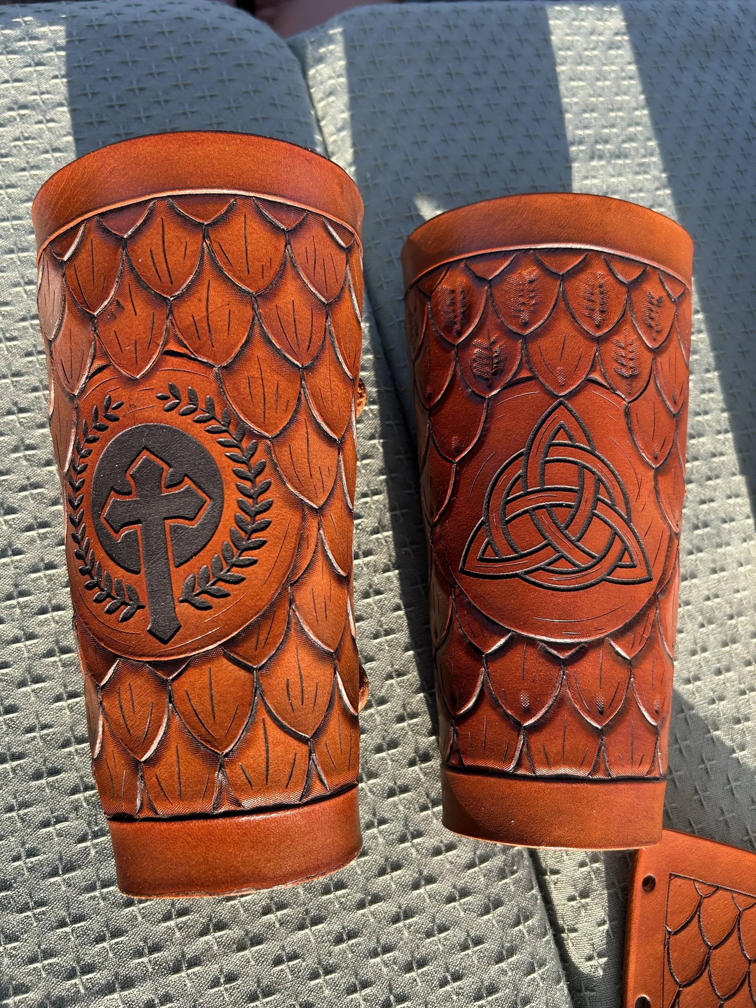 Close-up view of two orange leather wristbands with Viking and Celtic knot designs, placed on a textured gray surface.