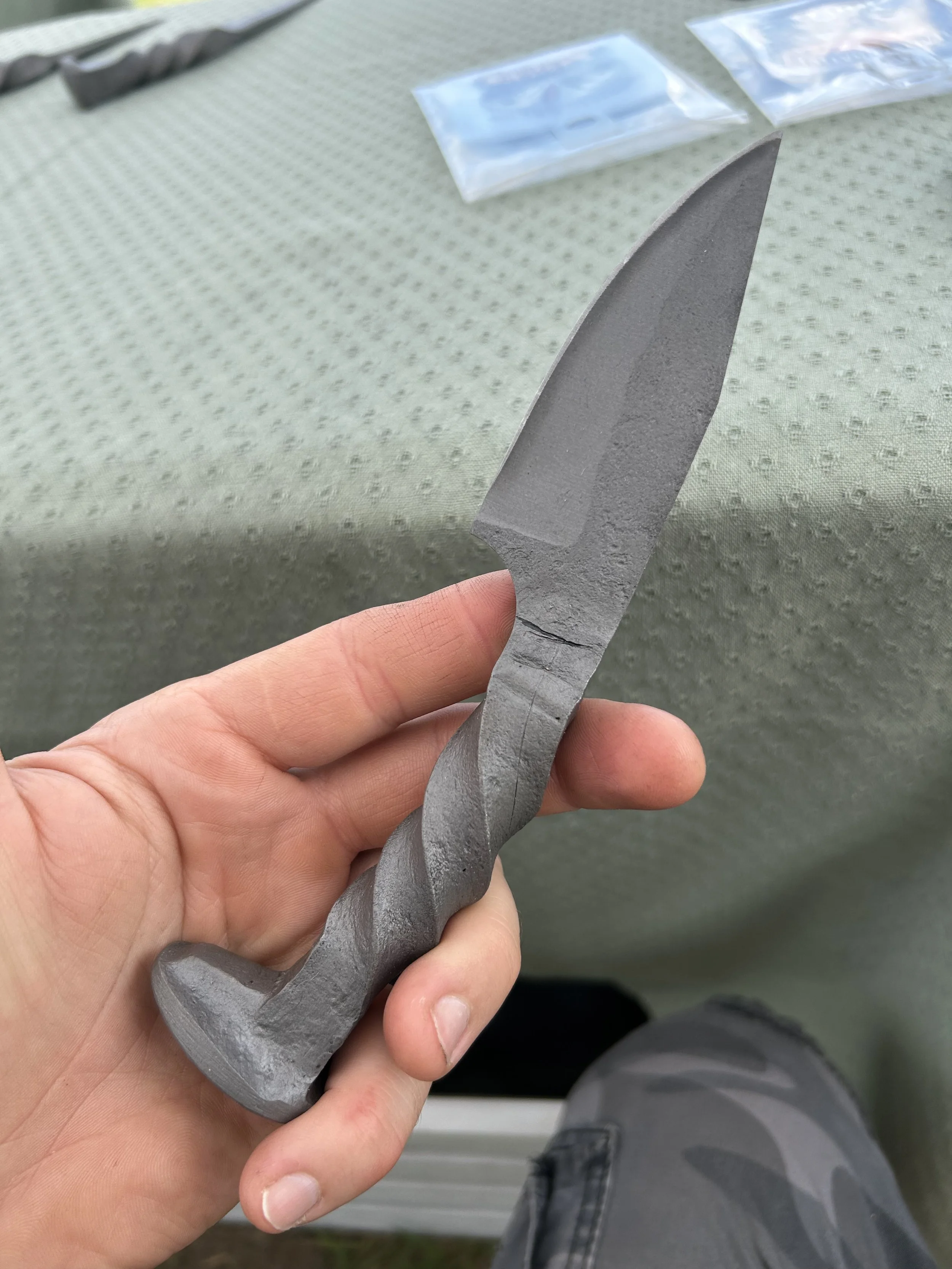Person holding a railroad spike knife with a twisted, decorative design, against a textured grey background.