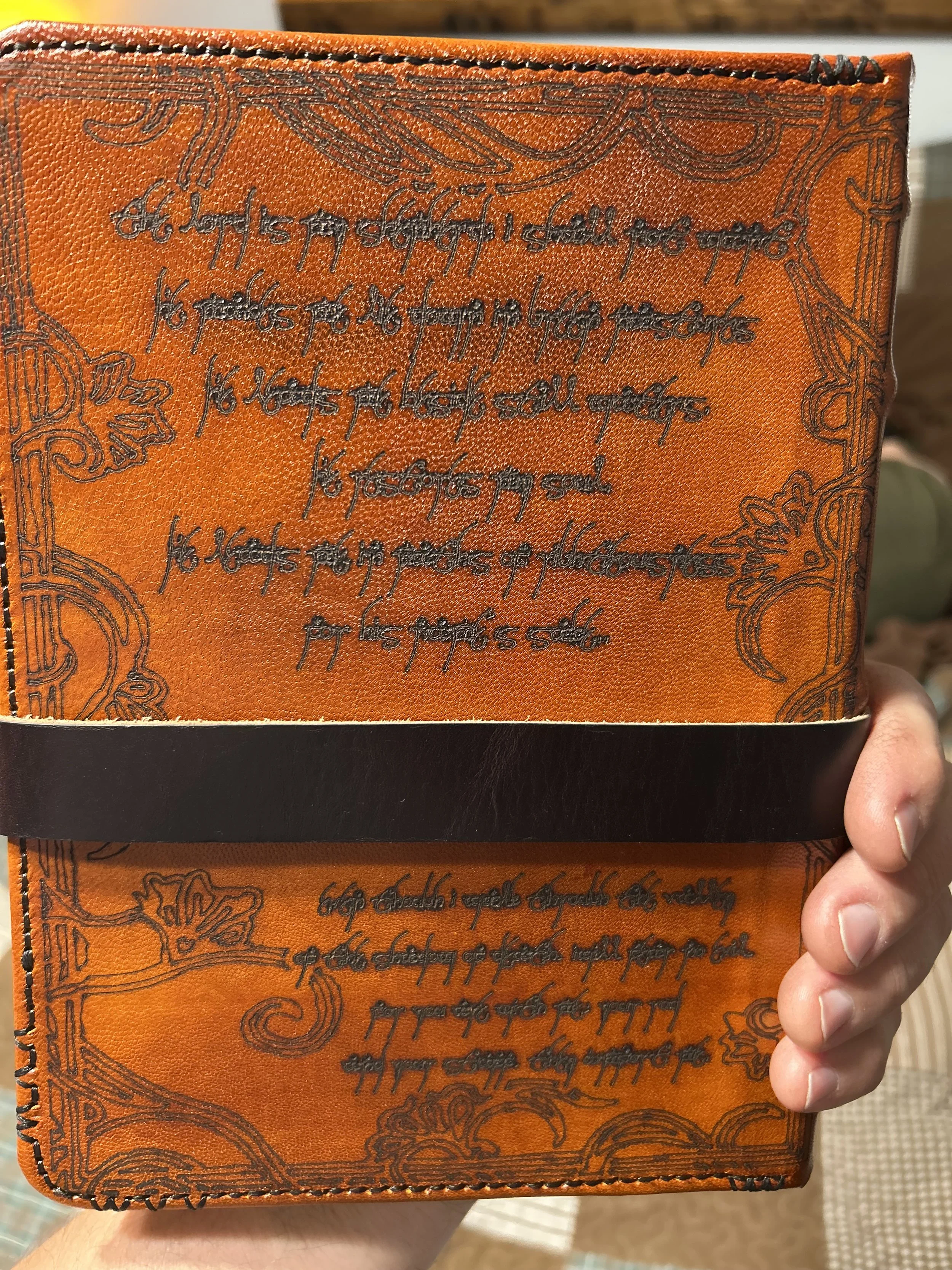 A person holding an orange wallet with black decorative designs and cursive writing on it, with a black bottom edge visible.