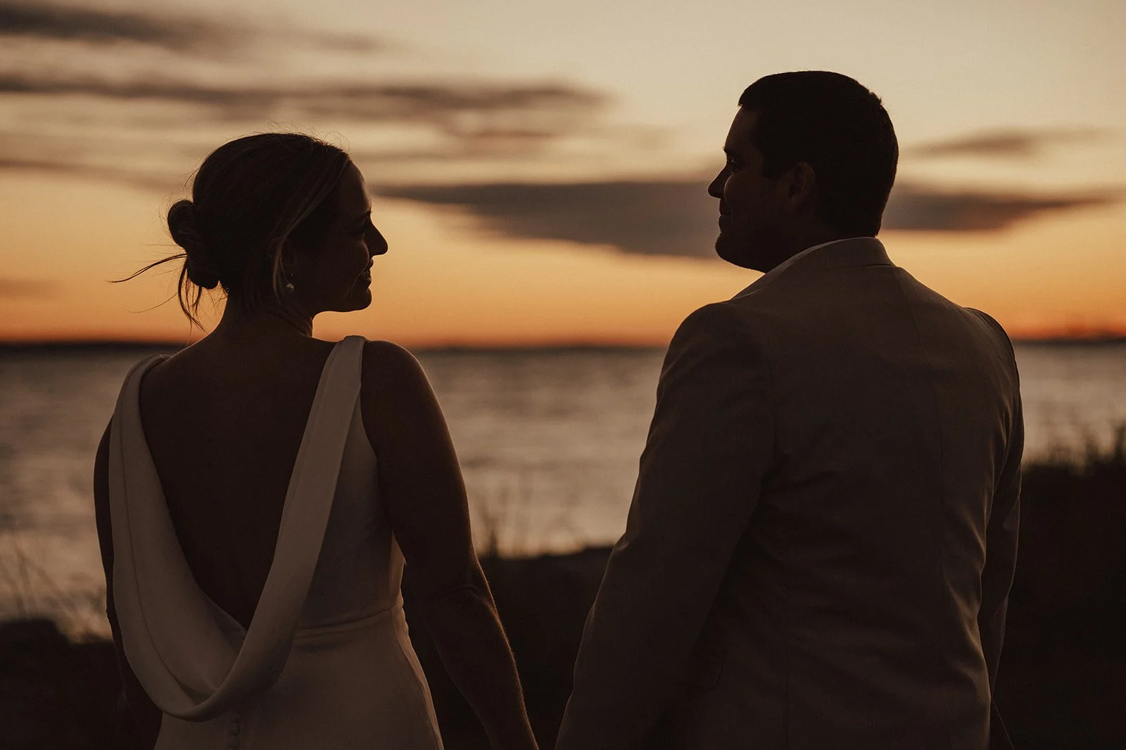 Silhouetted couple holding hands by the water at sunset.