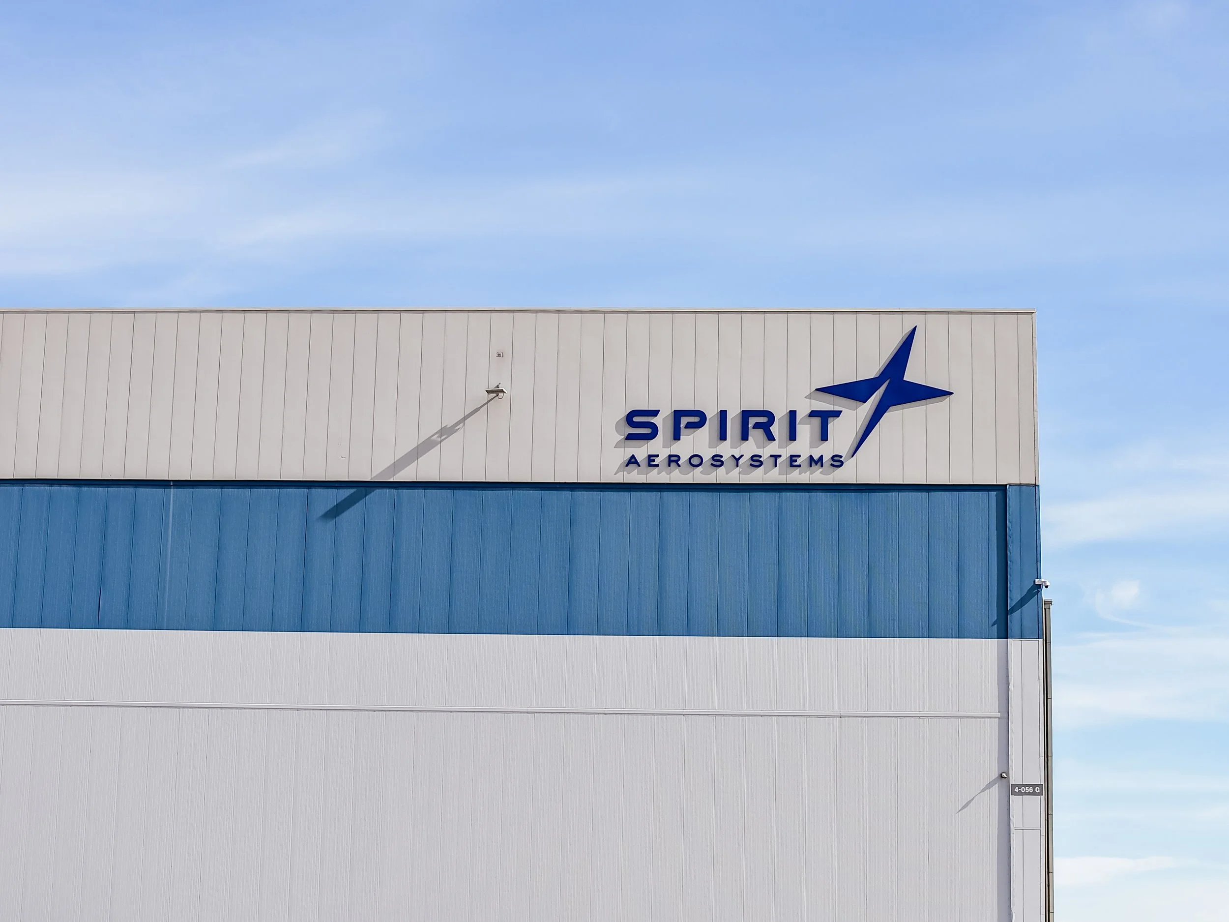 The exterior of a building with the sign 'Spirit Aerosystems' featuring a stylized airplane logo, blue and white color scheme, under a clear blue sky.
